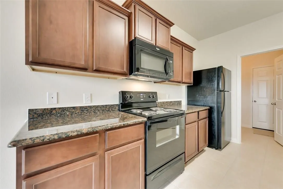 Kitchen featuring wood-finish cabinetry, speckled countertops, and a full suite of black appliances