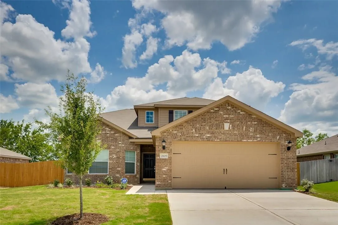 Brick veneer exterior with a two-car garage, concrete driveway, and a front entry featuring a transom window