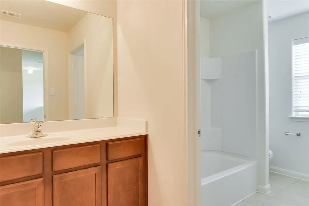 Bathroom featuring a wood-finish vanity with a white countertop, an integrated sink, and a large wall-mounted mirror