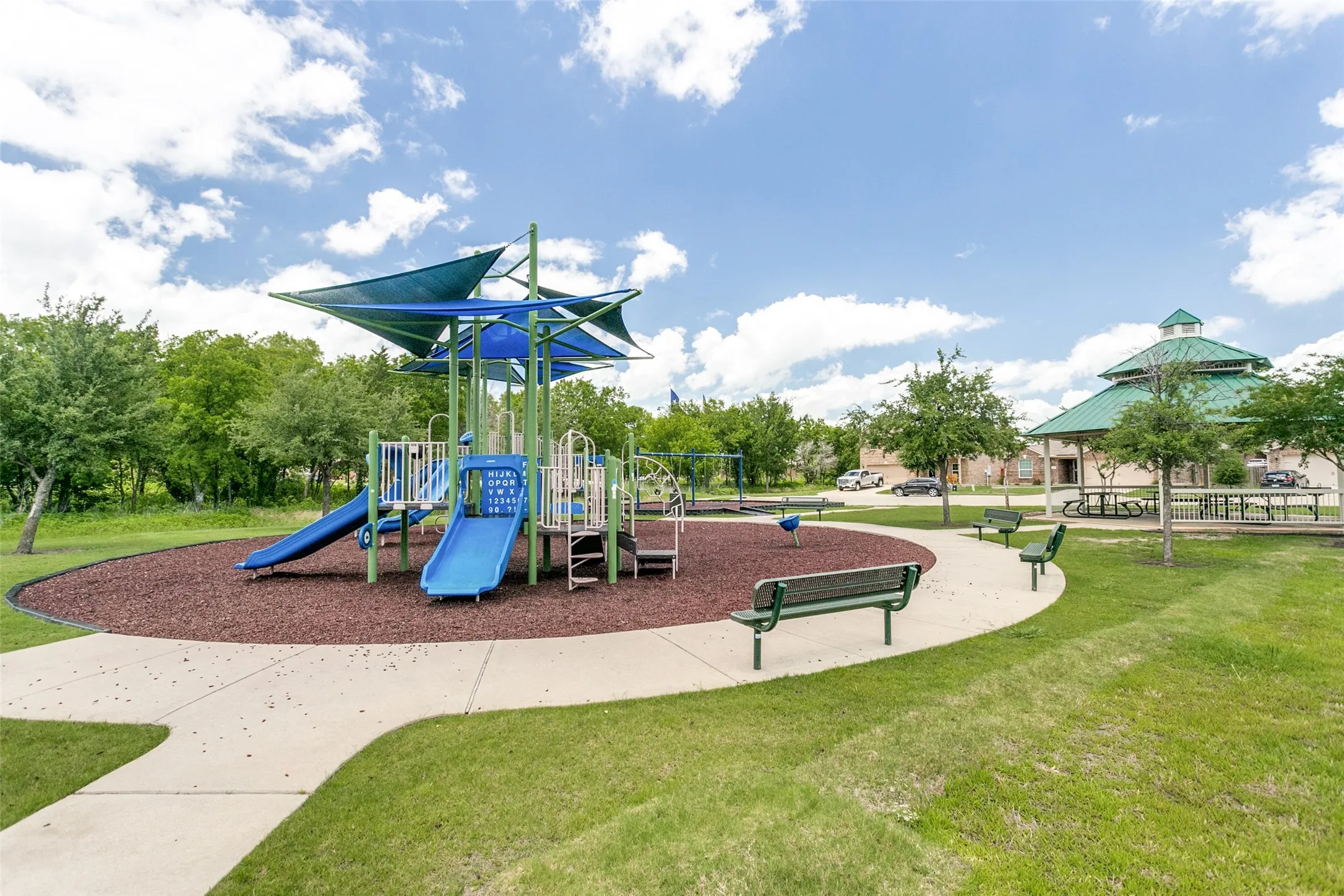 Community playground featuring a multi-level play structure with slides and swings, shaded by blue canopies