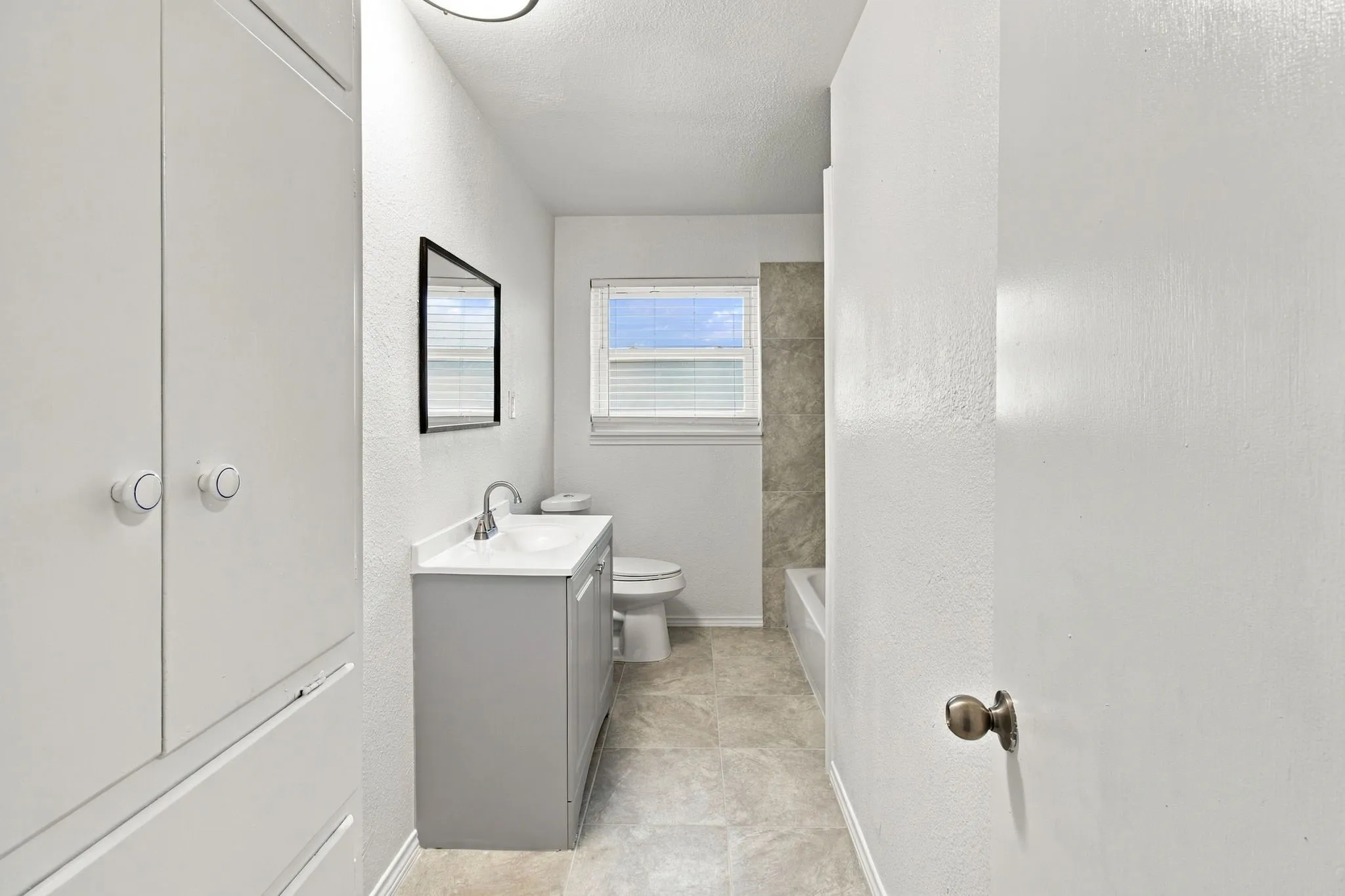 Bathroom featuring a vanity with an integrated sink, built-in storage cabinetry, tiled flooring, and a tiled bath surround