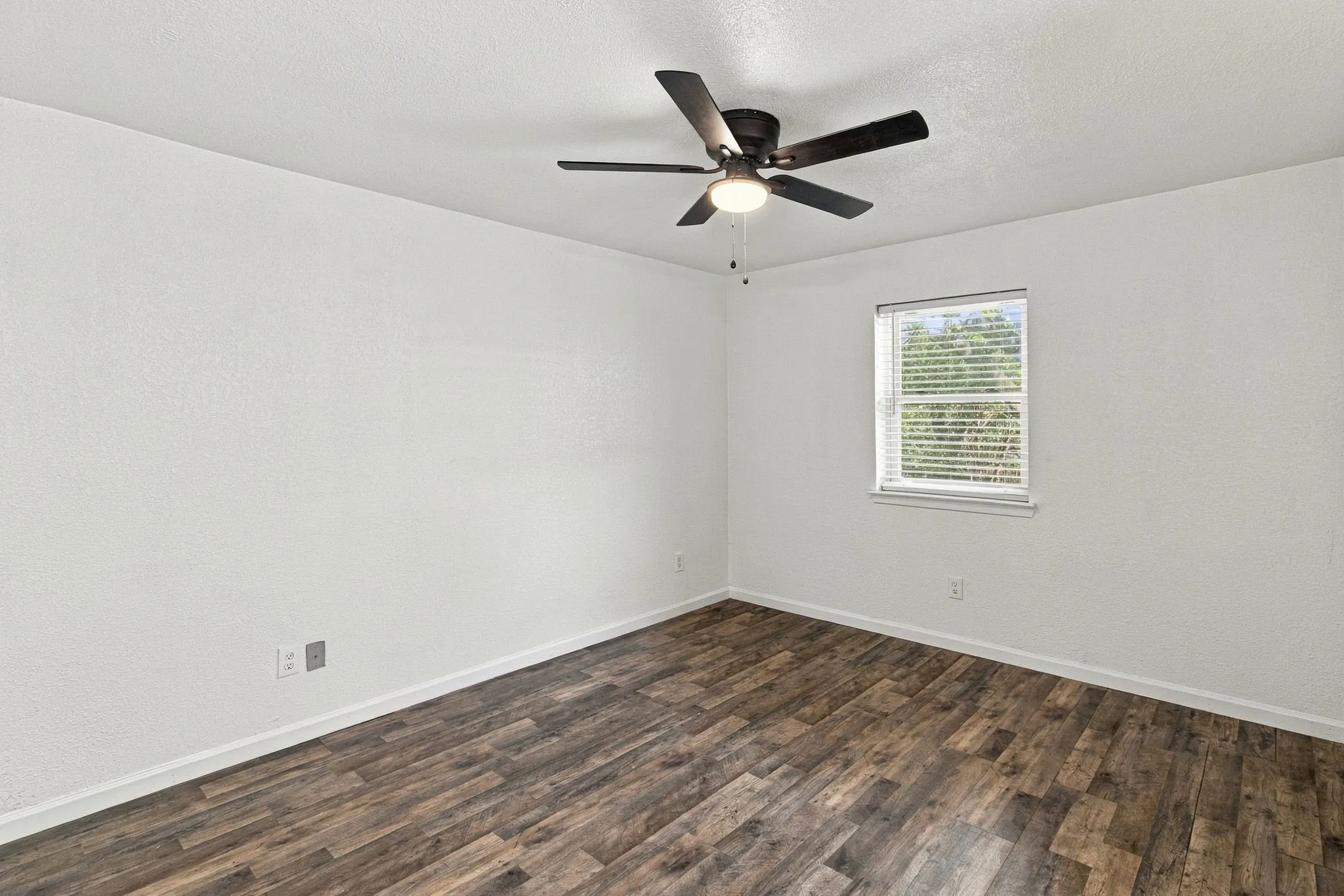 Room with wood-finish flooring, a ceiling fan with integrated lighting, and a window featuring blinds