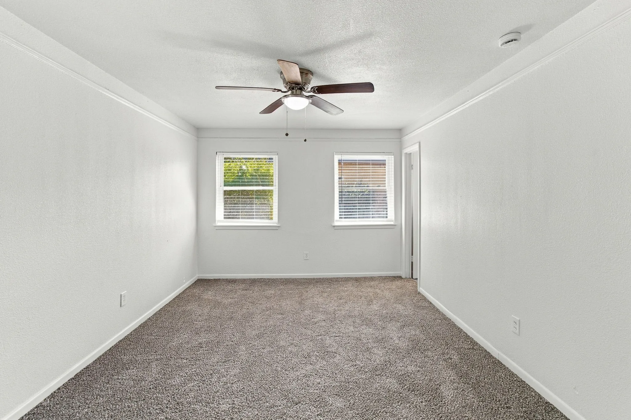 Textured carpeting, two windows with blinds, and a ceiling fan with integrated lighting