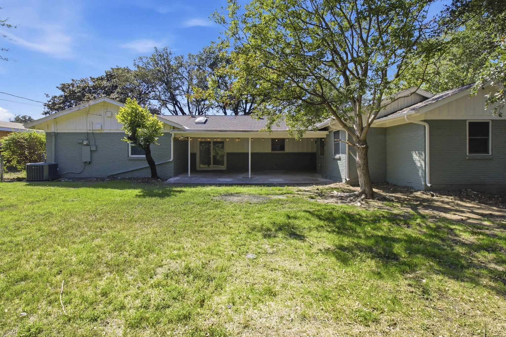 Expansive backyard featuring a covered patio, sliding glass doors, and mature trees