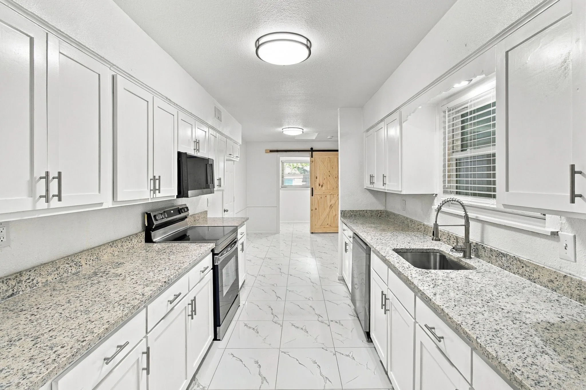 Galley kitchen with white shaker cabinetry, granite-style countertops, stainless steel appliances, and tile flooring