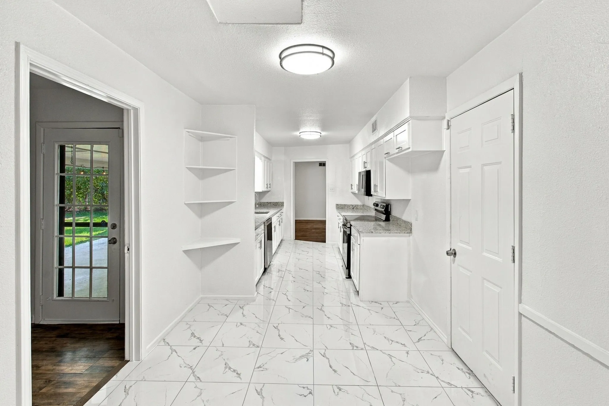 Galley kitchen featuring white cabinetry, light-toned countertops, and integrated appliances