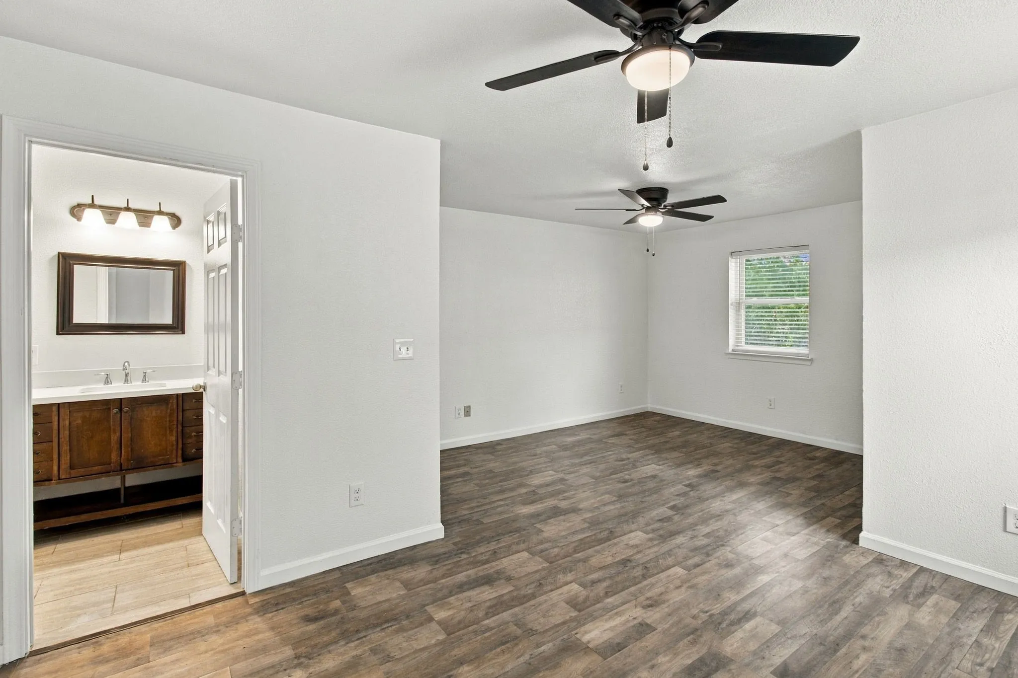 Spacious room featuring wood-finish flooring, two ceiling fans, and a window for natural light