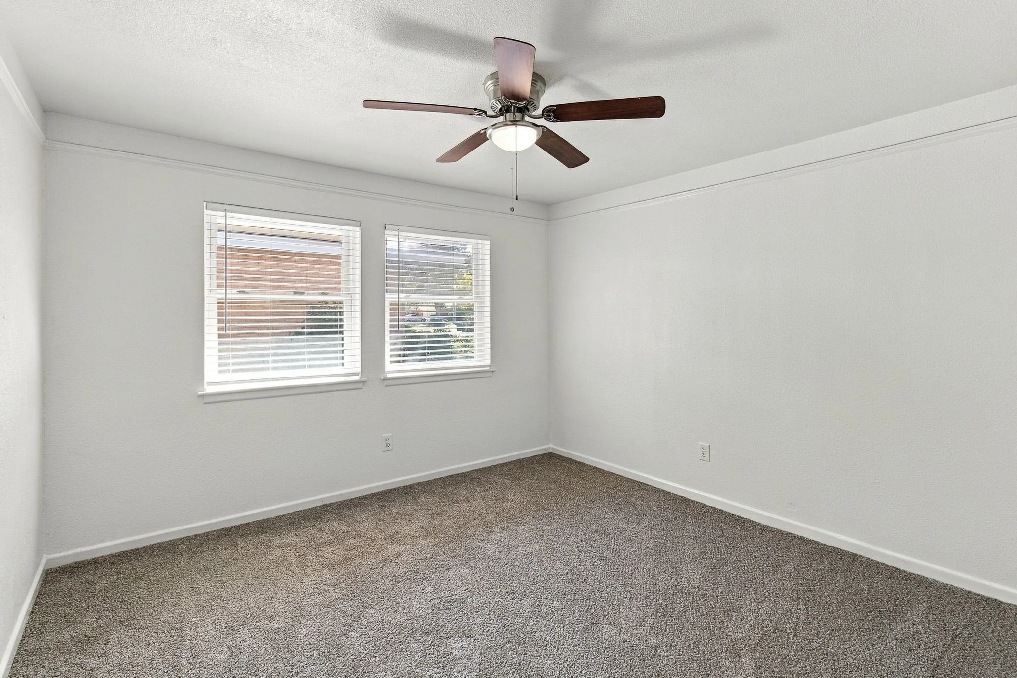 Neutral wall color, two windows with blinds, crown molding, ceiling fan with integrated lighting, and carpeted flooring