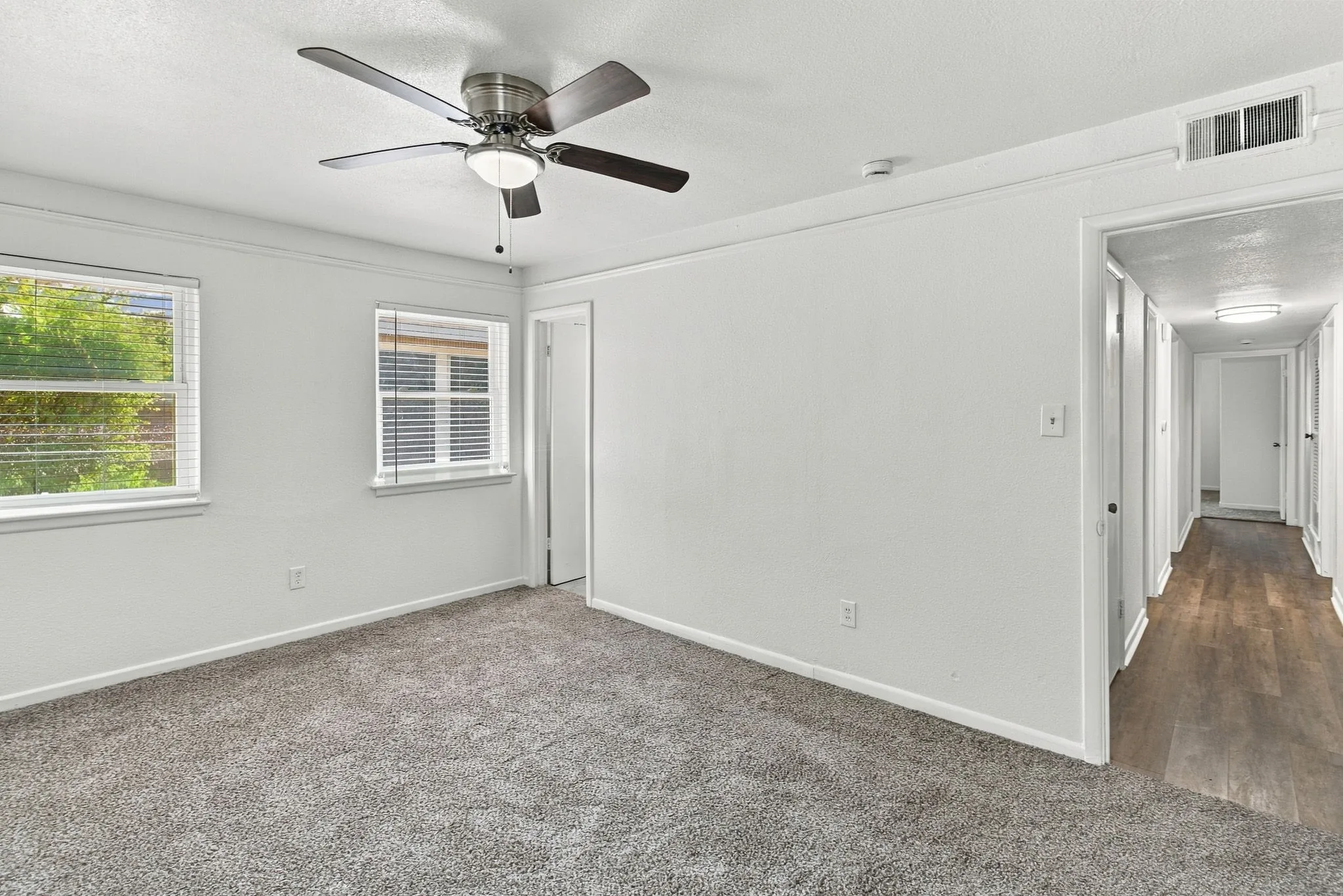Room featuring gray carpeting, white walls, two windows with blinds, and a ceiling fan