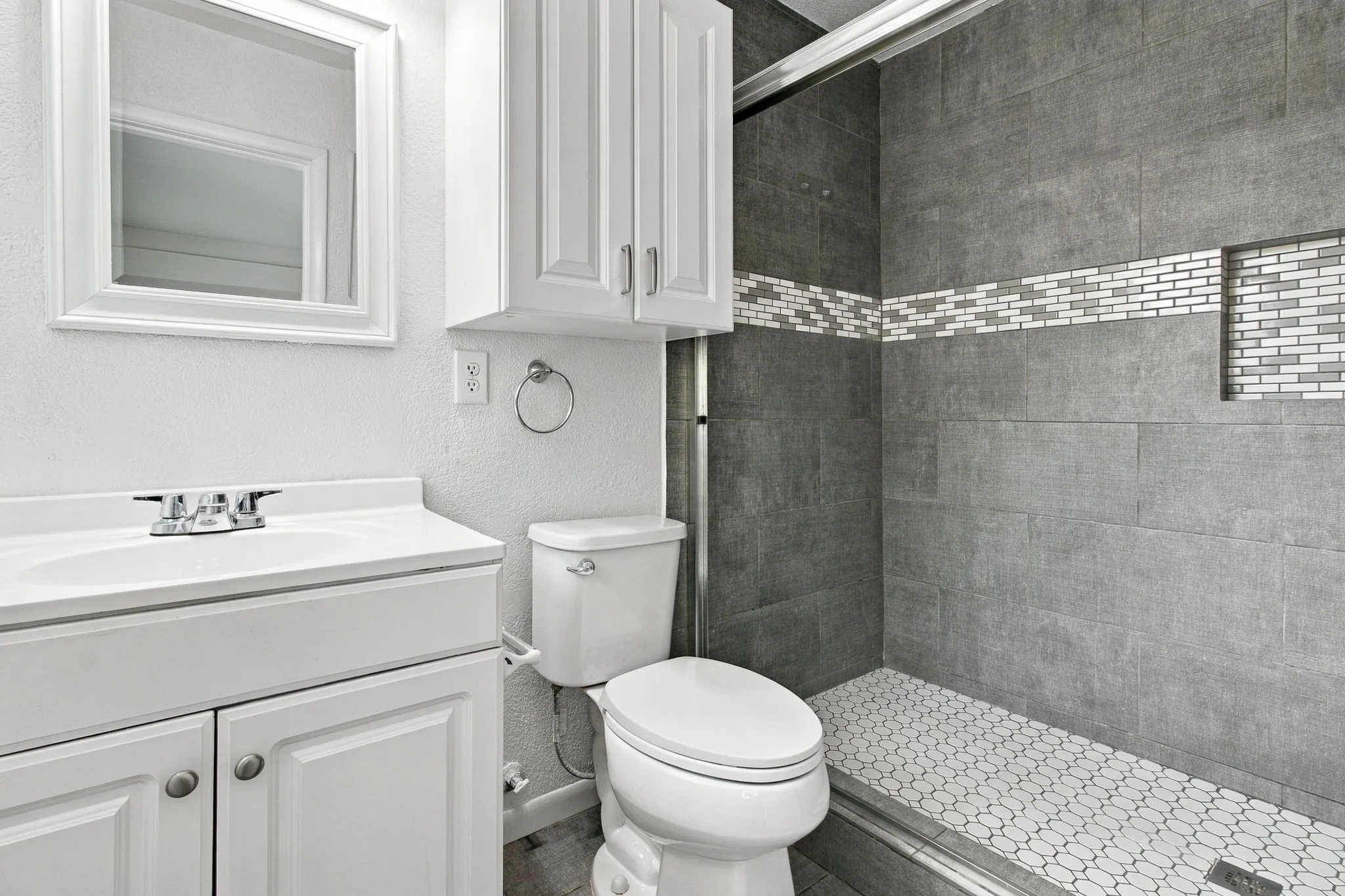 Bathroom featuring a modern vanity with integrated sink, white shaker cabinetry, tiled shower with mosaic accent band, and built-in shower niche