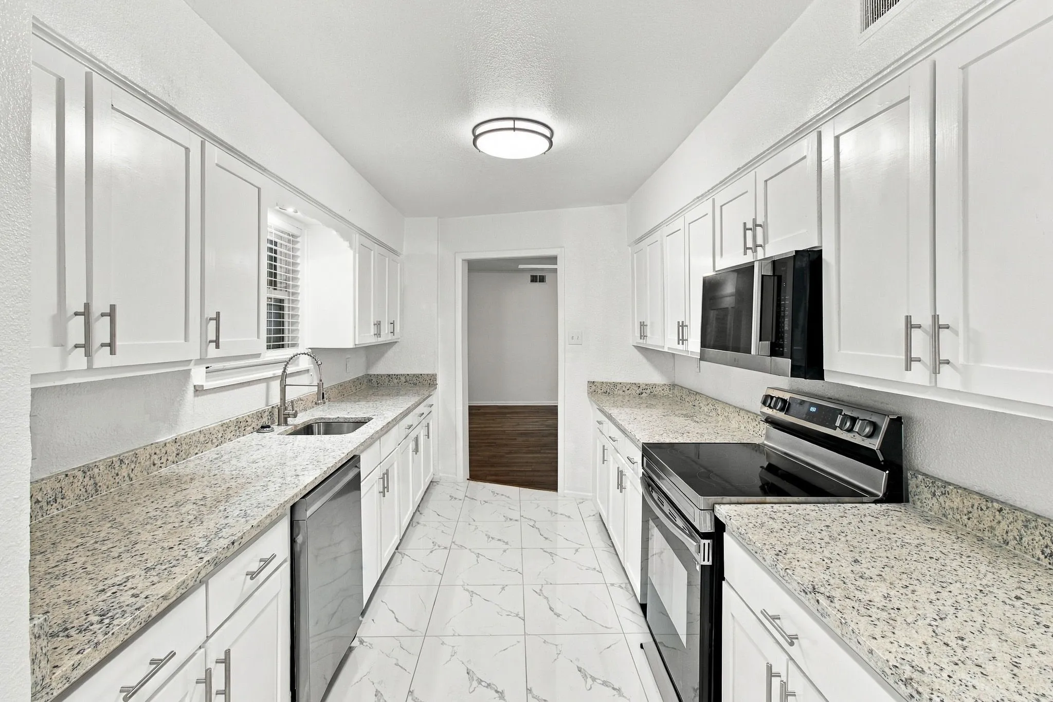 Galley kitchen featuring white cabinetry, light-toned countertops, tile flooring, and integrated stainless steel appliances