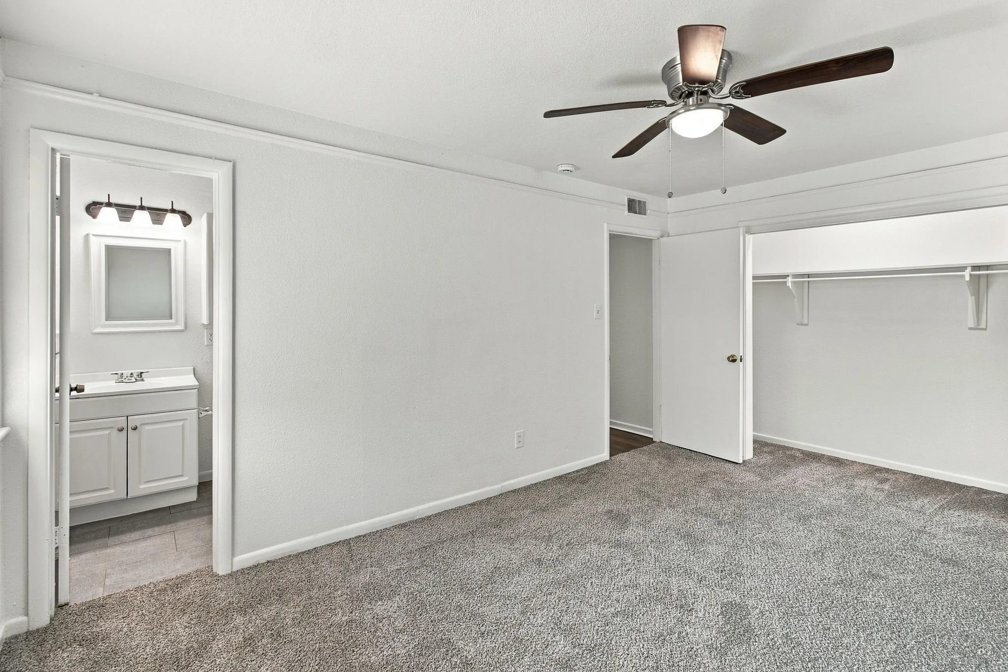 Carpeted room with ceiling fan, white walls, and a built-in closet with shelving and hanging rod