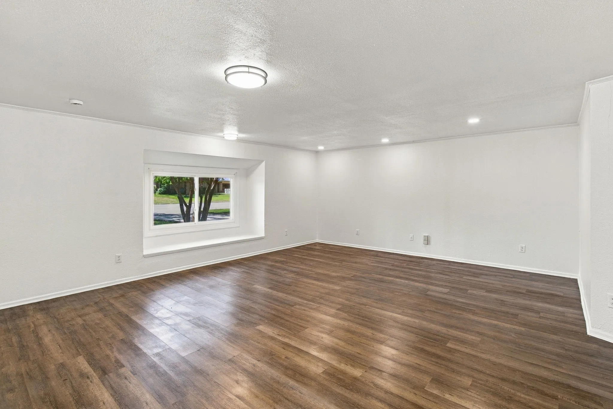 Spacious room featuring wood-finish flooring, recessed lighting, and a prominent window