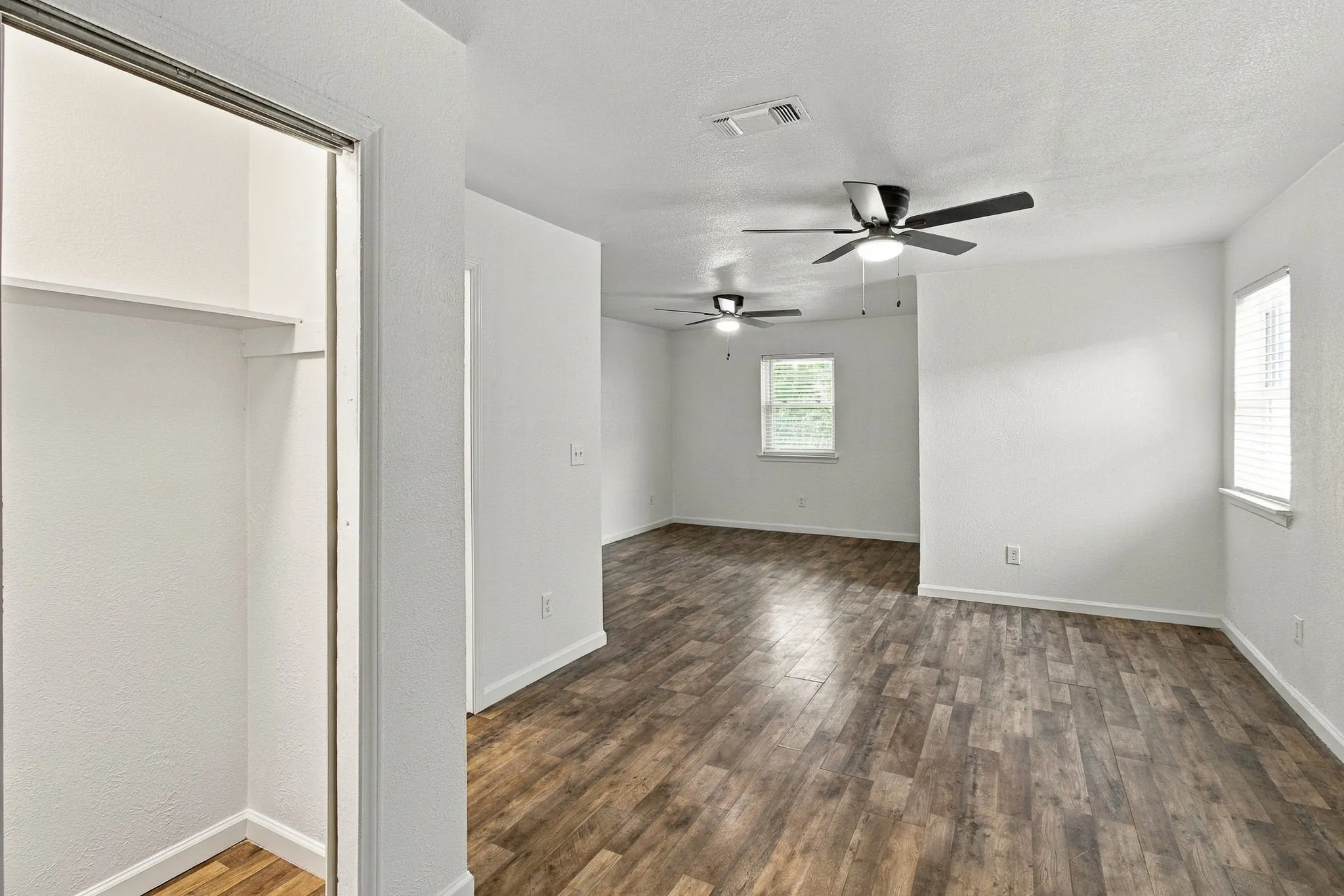Spacious interior featuring wood-finish flooring, two ceiling fans, multiple windows with blinds, and an open closet with shelving