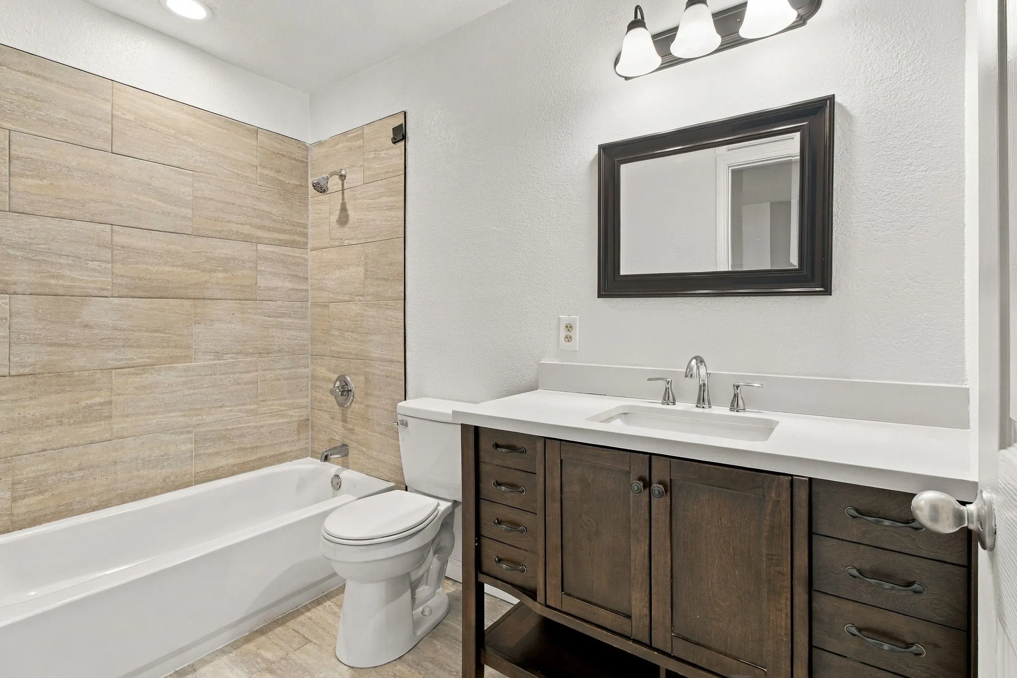 Bathroom featuring a tiled shower surround, integrated bathtub, and a dark wood-finish vanity with a white countertop