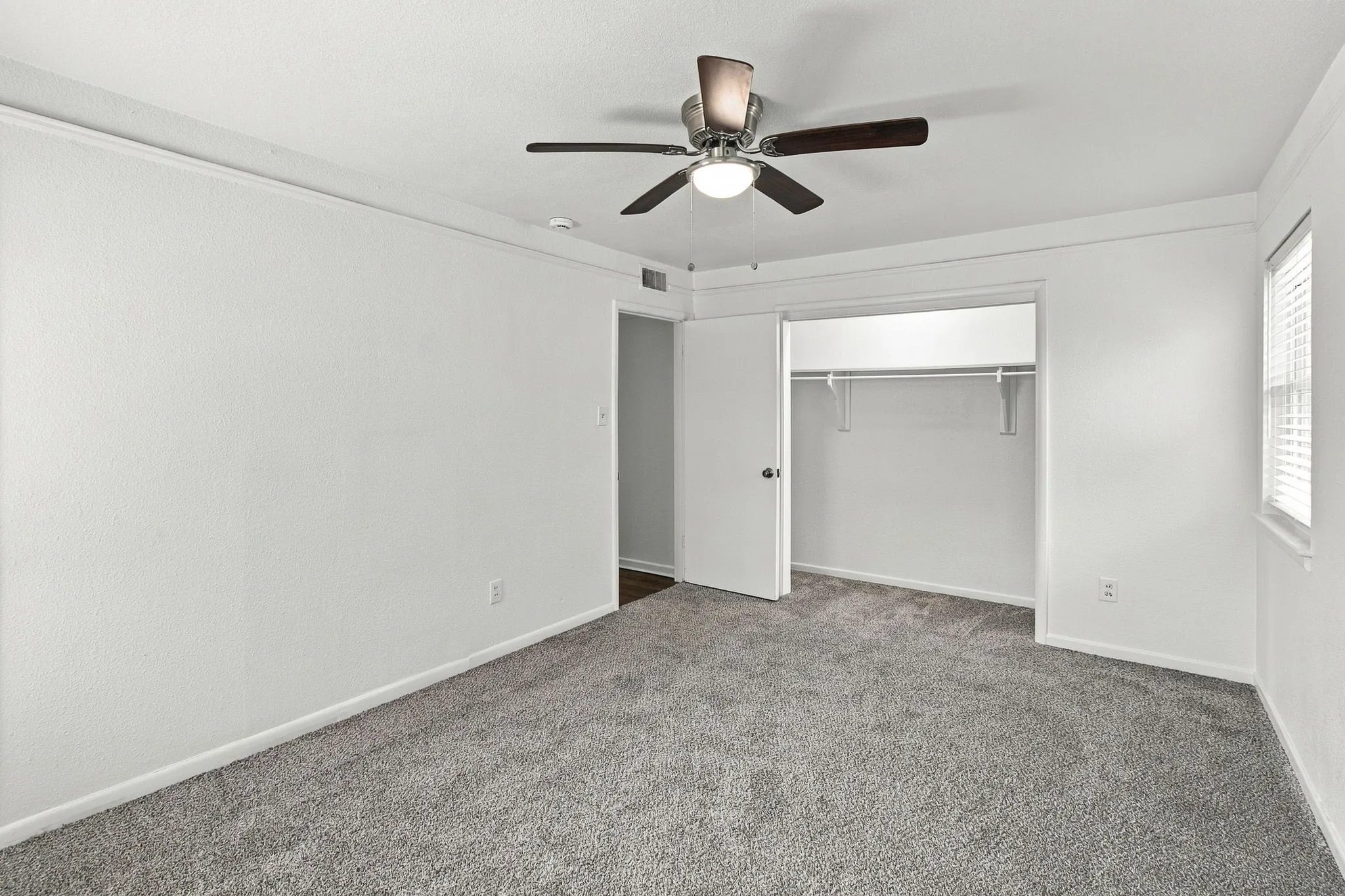 Wall-to-wall carpeting, overhead ceiling fan with integrated lighting, window with blinds, and built-in closet with shelving and hanging rod