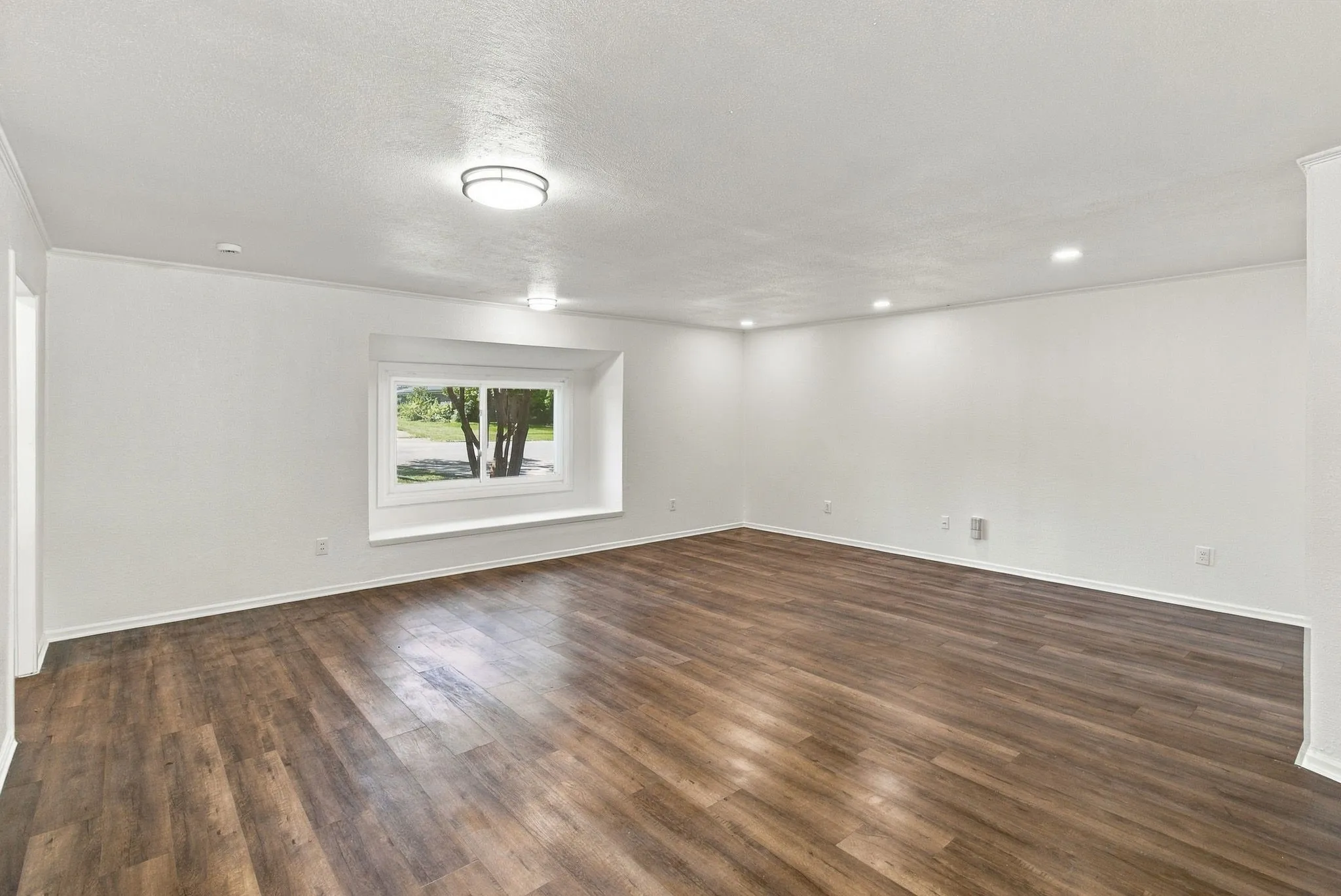 Spacious room featuring wood-finish flooring, recessed lighting, a large window, and crown molding