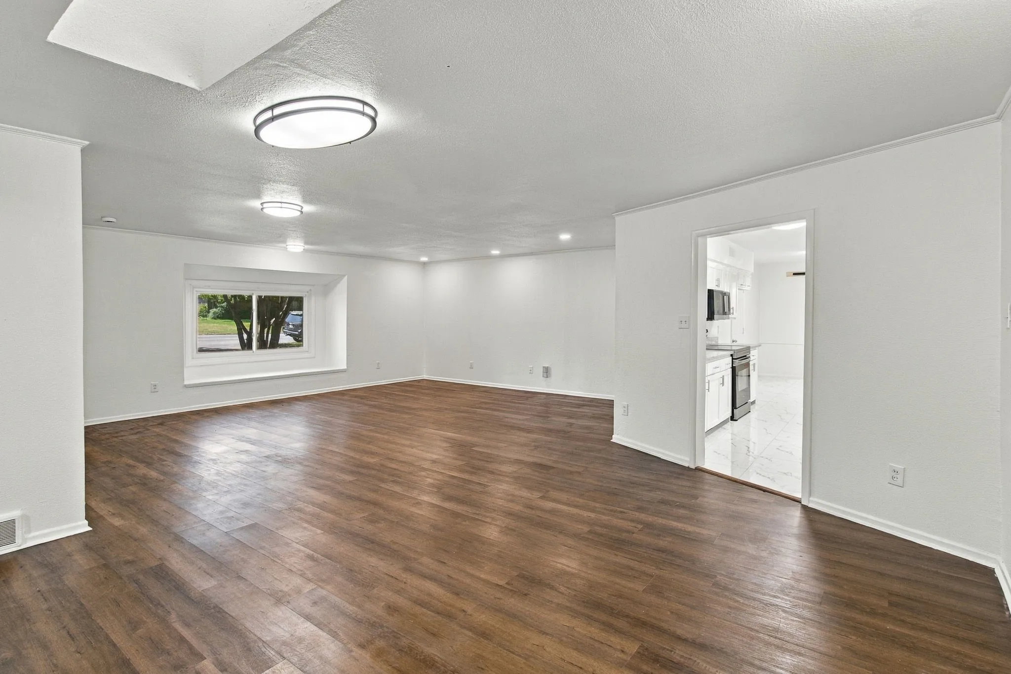 Spacious living area featuring wood-finish flooring, recessed lighting, and a prominent window ledge