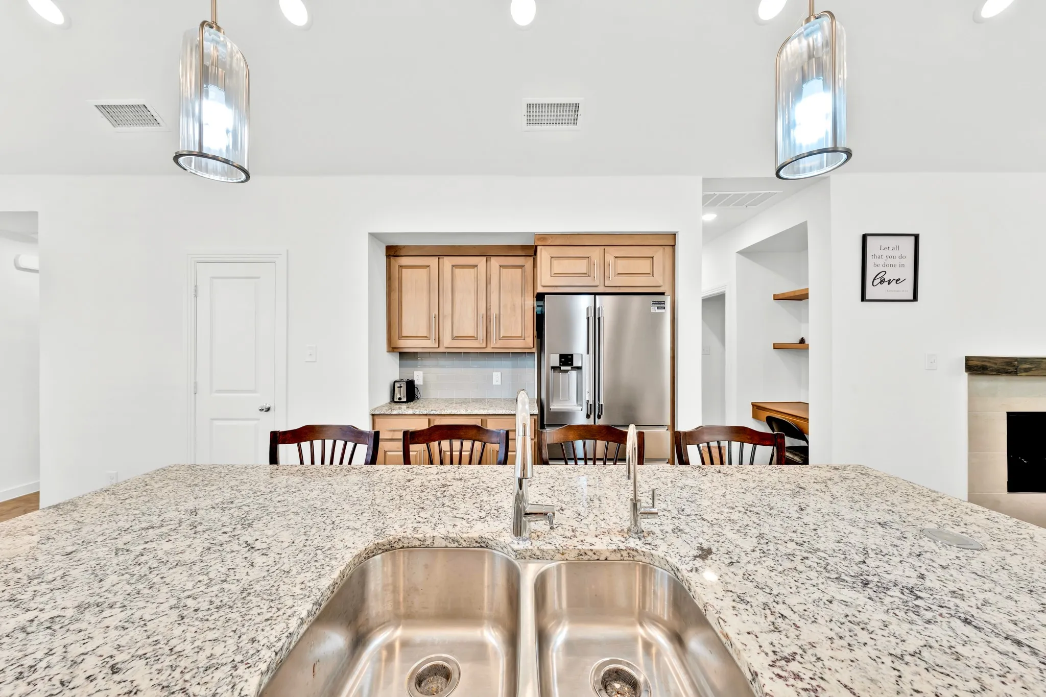 Kitchen island with a double stainless steel sink and granite countertop, stainless steel refrigerator, and wood cabinetry