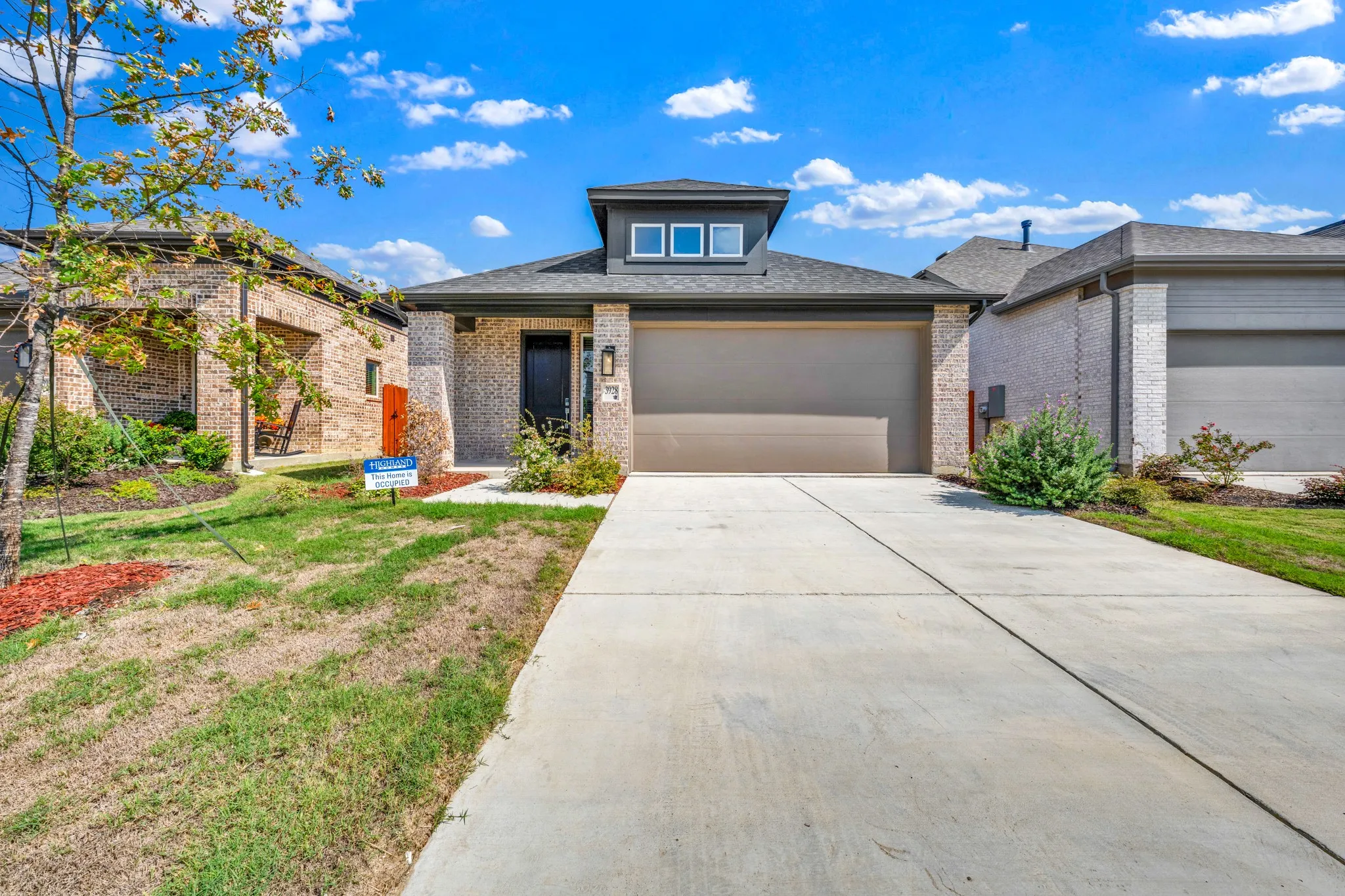 Brick facade with a contrasting dark front door, attached garage, and concrete driveway
