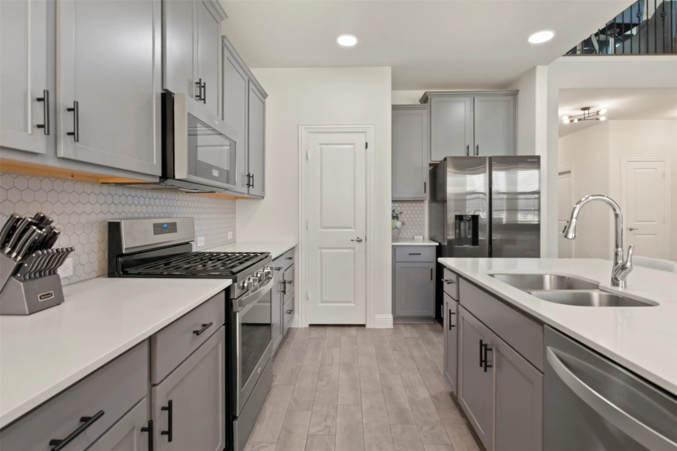 Contemporary kitchen featuring light gray cabinetry, white countertops, wood-finish flooring, and stainless steel appliances including a gas range and refrigerator