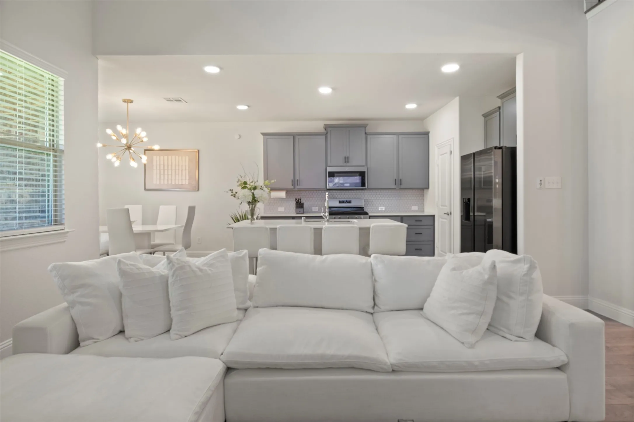 Recessed lighting, wood-finish flooring, light gray cabinetry, white tile backsplash, and a kitchen island with seating
