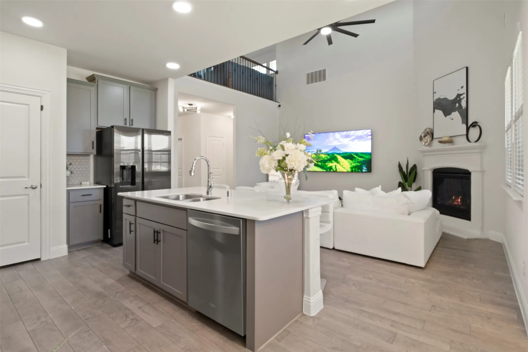 Open-concept living space with wood-finish flooring, a kitchen island featuring a double-basin sink, and gray cabinetry
