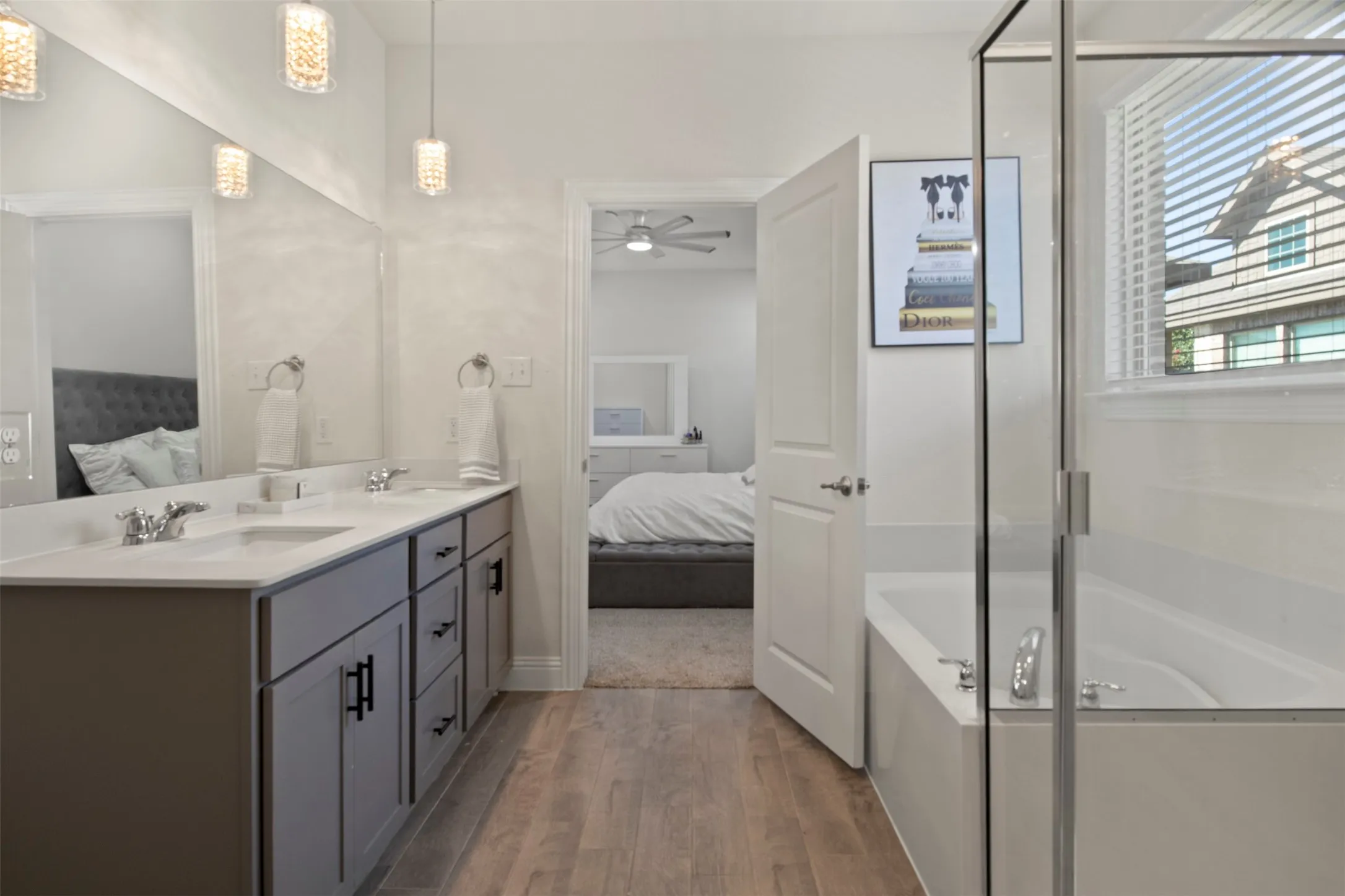 Dual sink vanity with dark wood-finish cabinetry, light countertops, wood-finish flooring, and a built-in soaking tub with glass enclosure