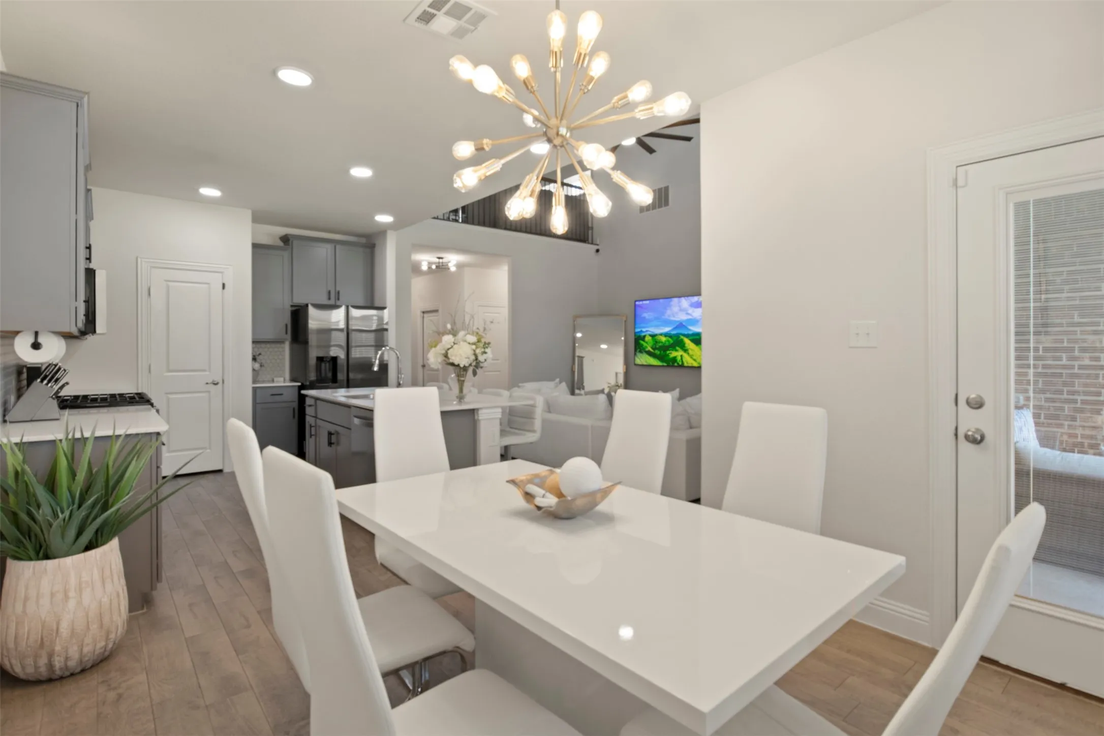 Open-concept dining and kitchen space featuring wood-finish flooring, a contemporary chandelier, recessed lighting, and a kitchen island with sink