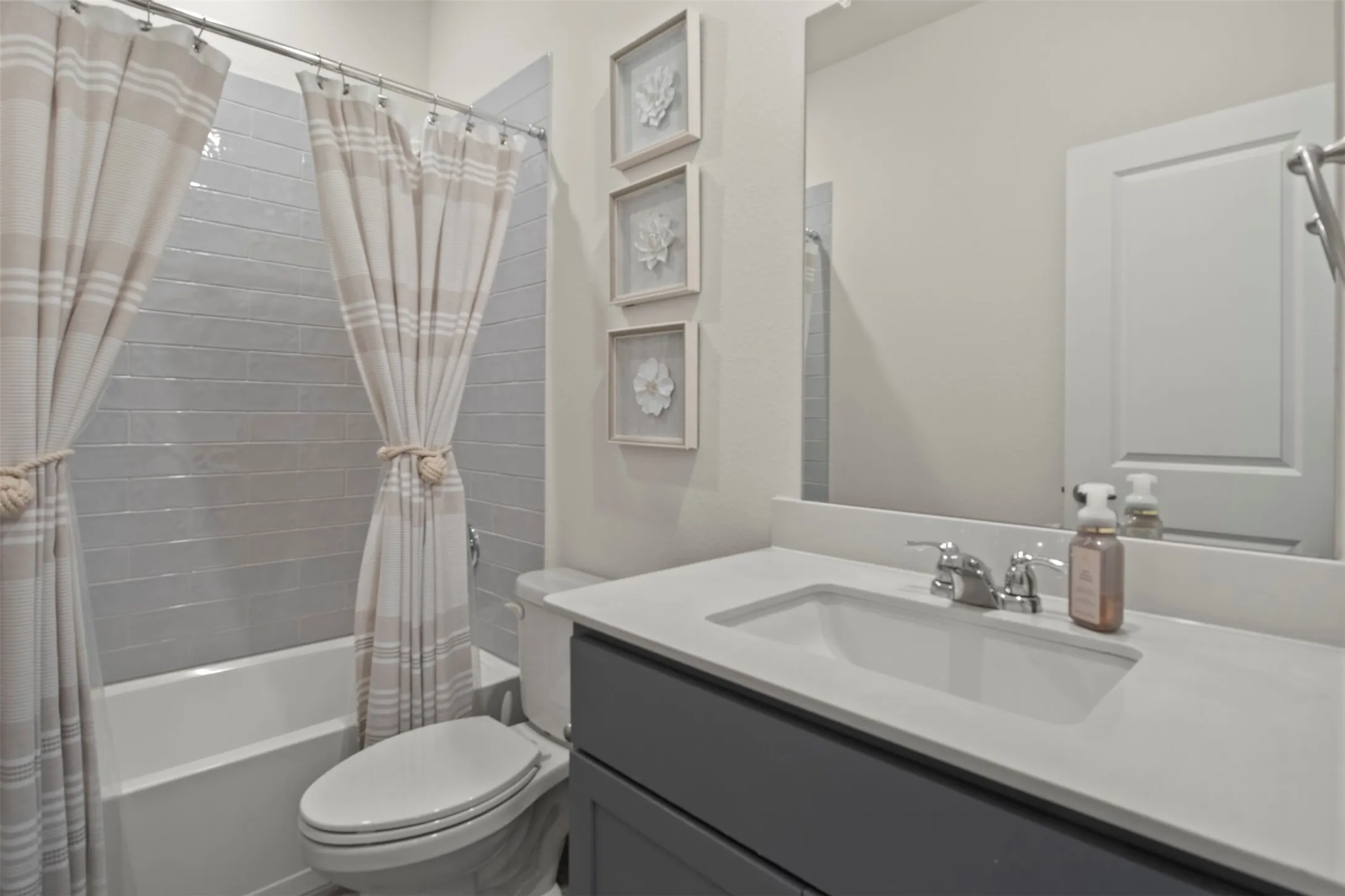 Bathroom featuring a white bathtub with subway tile surround, white toilet, and a vanity with a white countertop and rectangular sink