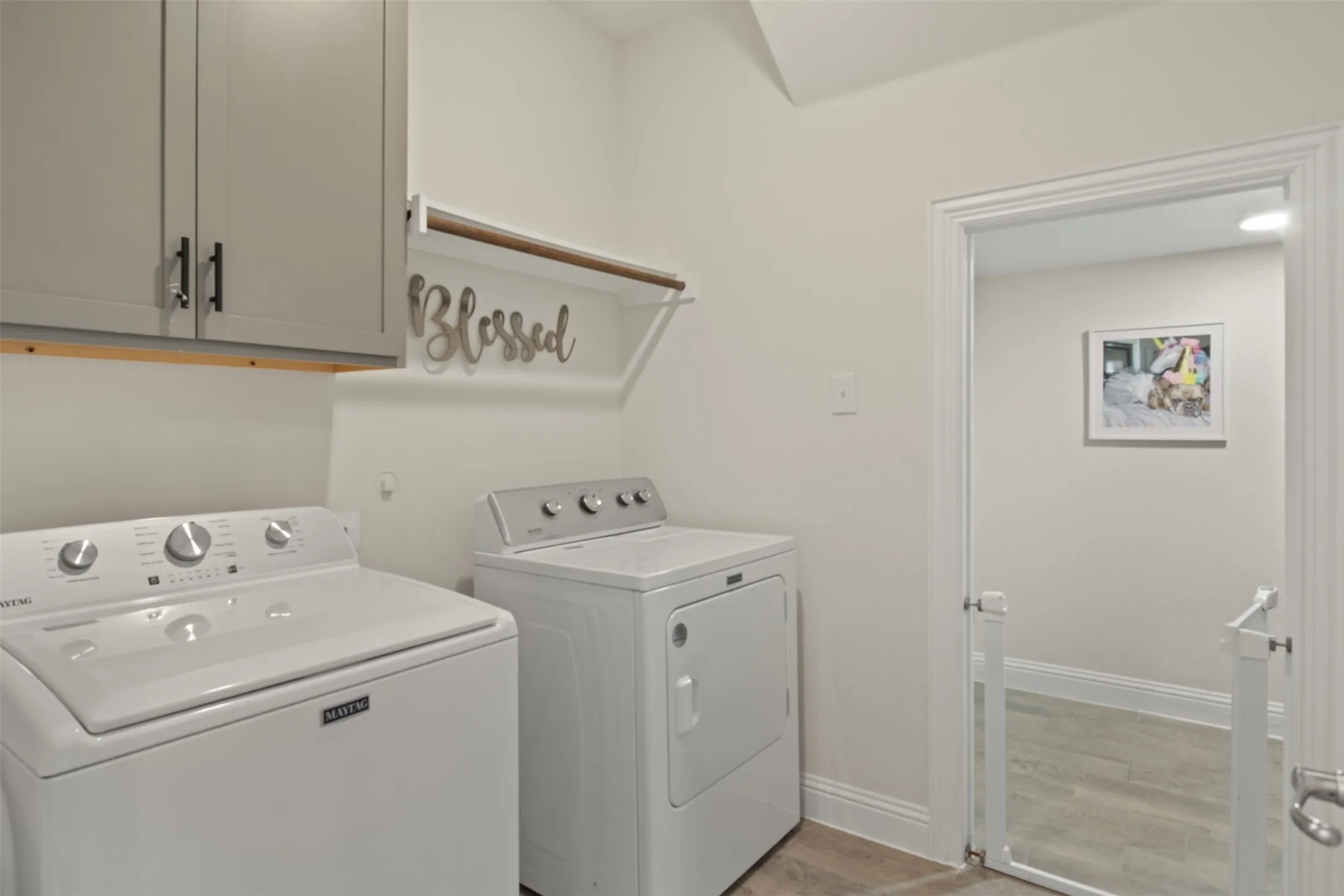 Laundry area with light gray cabinetry, wall-mounted shelving, wood-finish flooring, and white walls