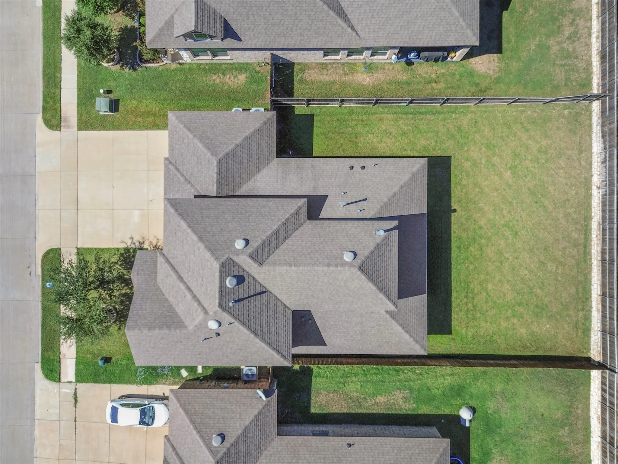 Pitched shingle roof with multiple gables, extensive concrete driveway, and a fenced perimeter
