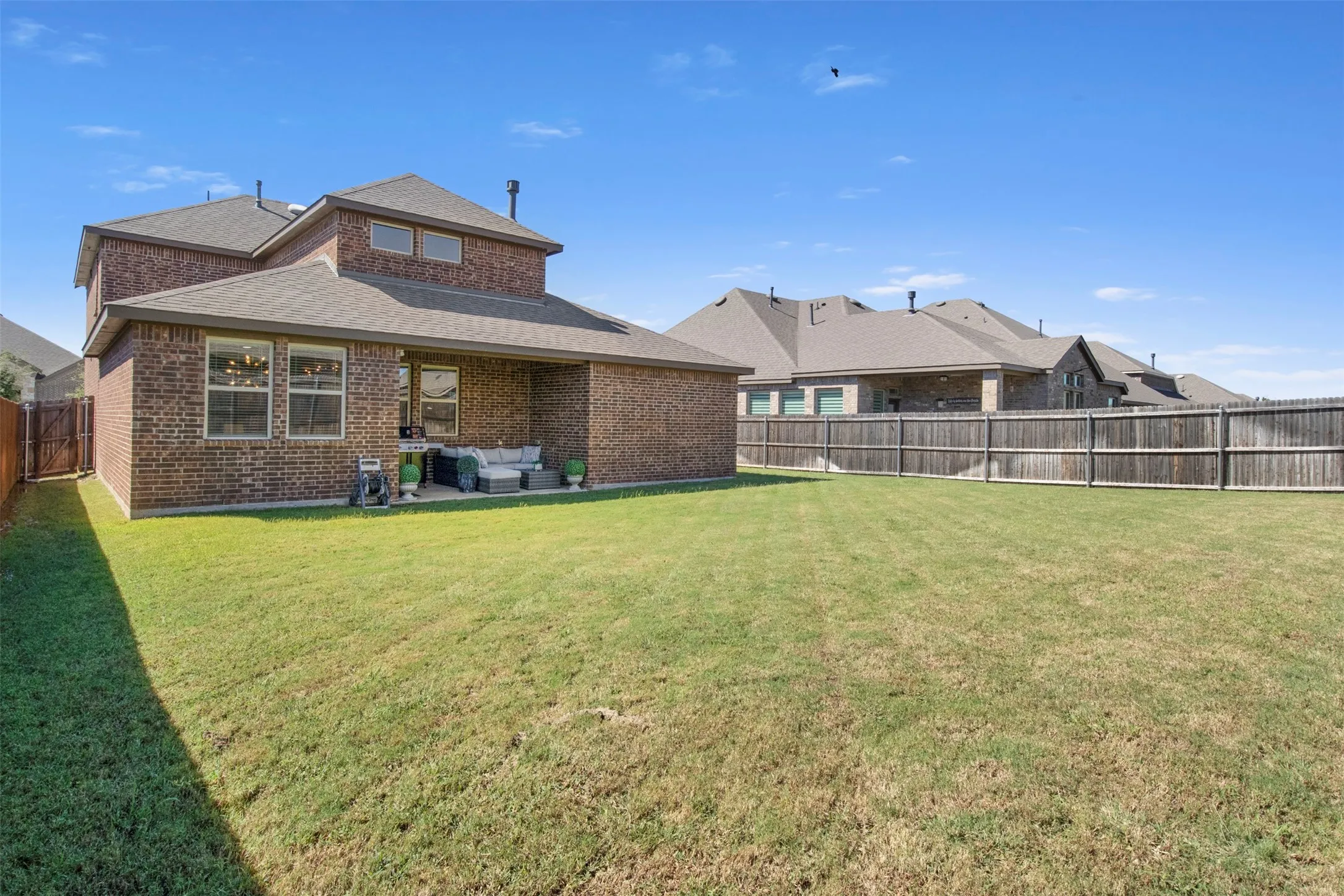 Expansive backyard featuring a large grass lawn, full privacy fencing, and a covered patio area with a concrete surface