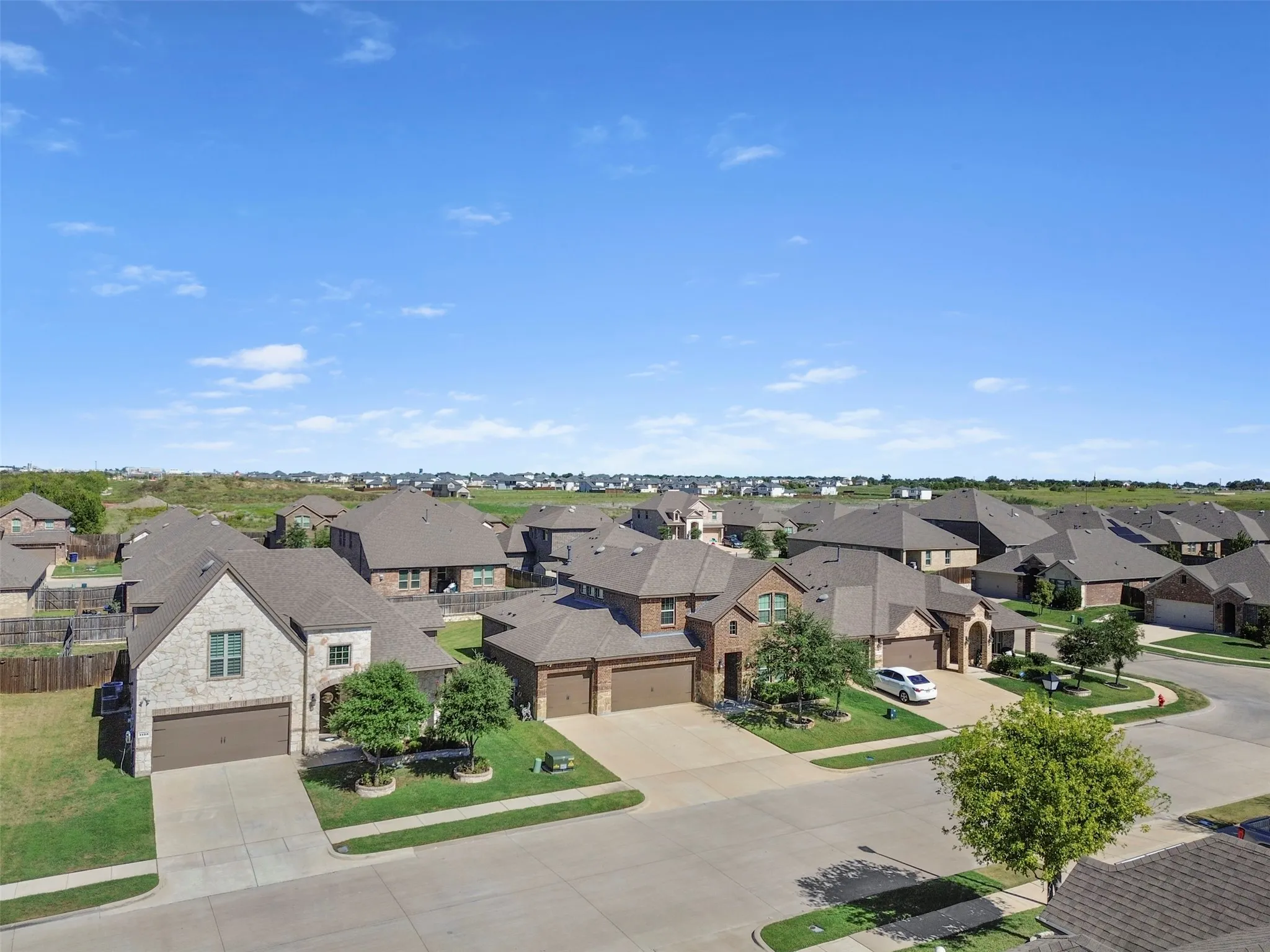 Residential street with multiple properties featuring brick and stone exteriors, attached garages, and manicured lawns