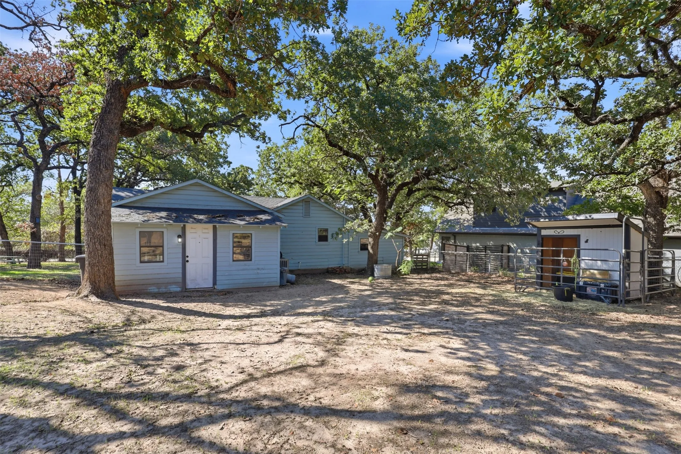Property features a light blue exterior, white door, and multiple mature trees