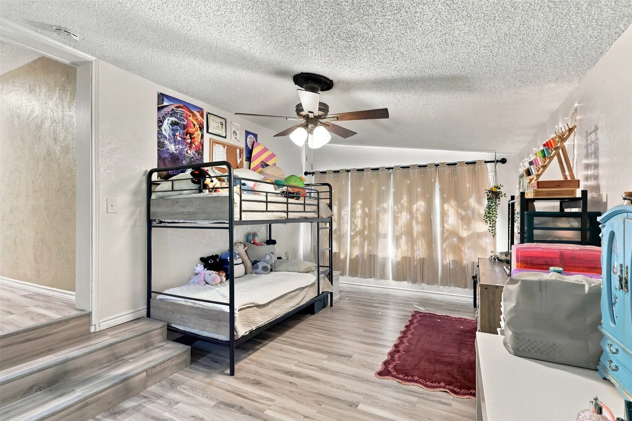 Wood-finish flooring throughout, ceiling fan with light fixture, and window with light-filtering curtains