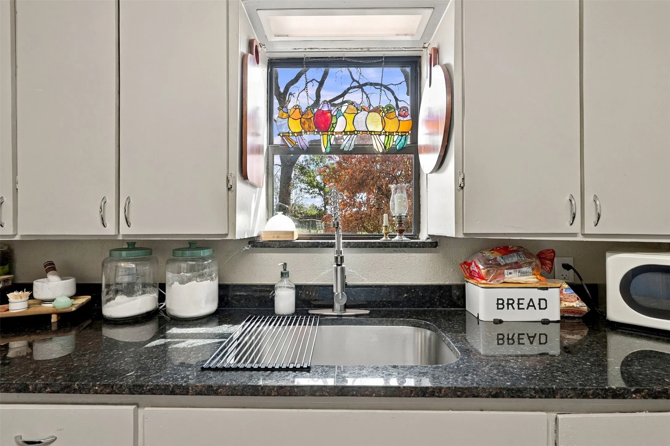 White cabinetry with chrome hardware, black speckled countertops, stainless steel sink, and a decorative stained-glass window