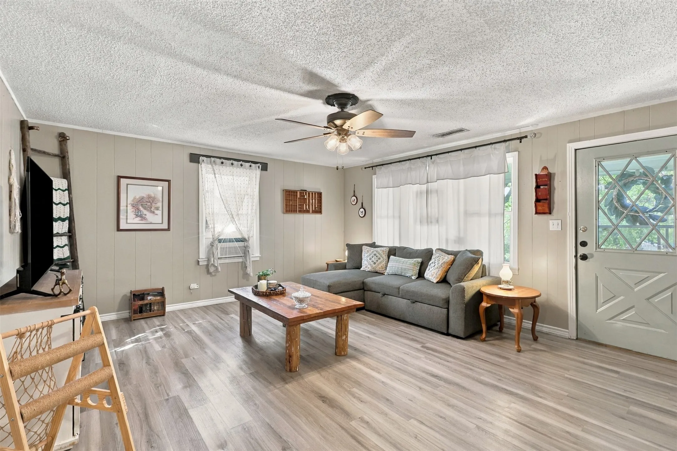 Spacious living area featuring wood-finish flooring, a ceiling fan with integrated lighting, and multiple windows