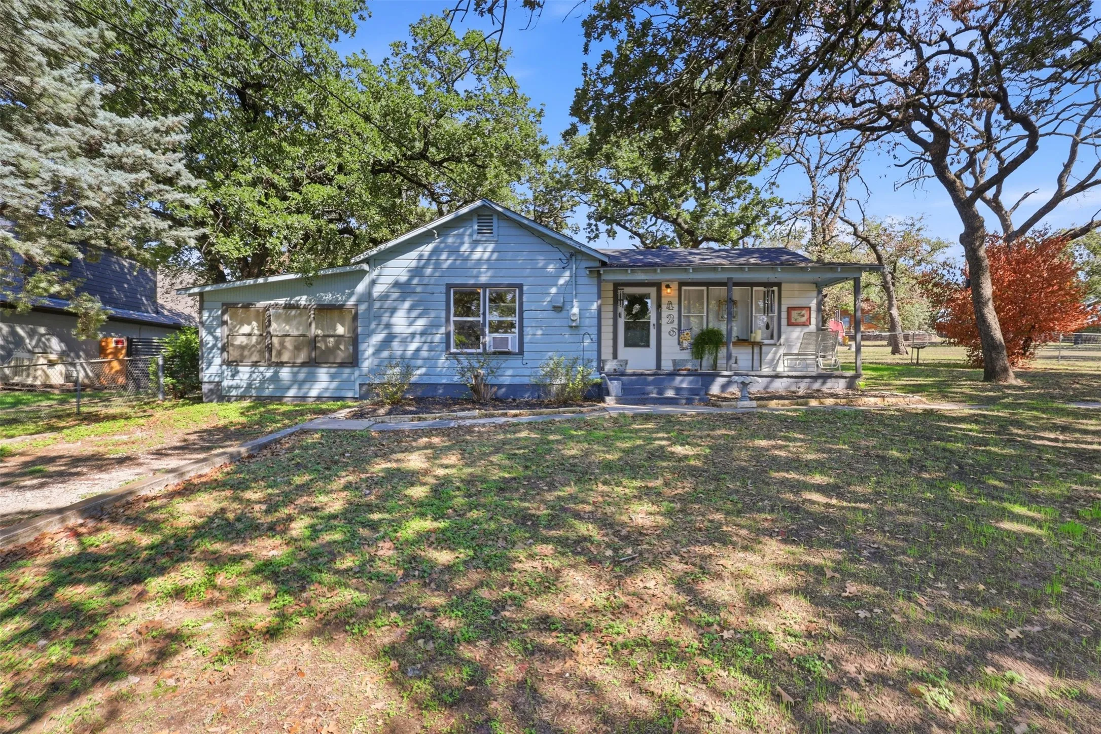Blue exterior siding, covered front porch with white columns, concrete porch steps, and a gravel driveway