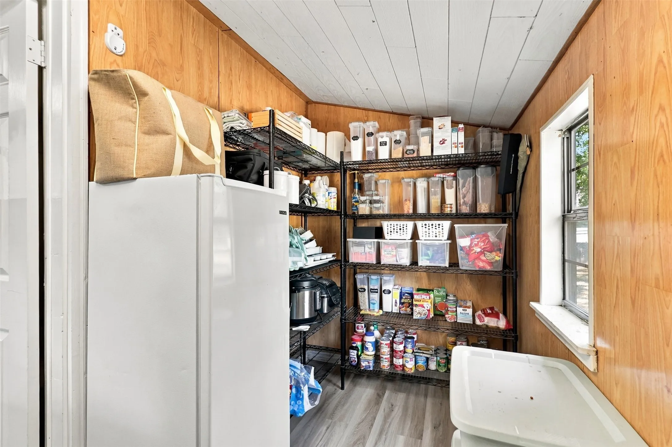 Wood-panel walls, multiple-tier wire shelving, wood-finish flooring, and a single window