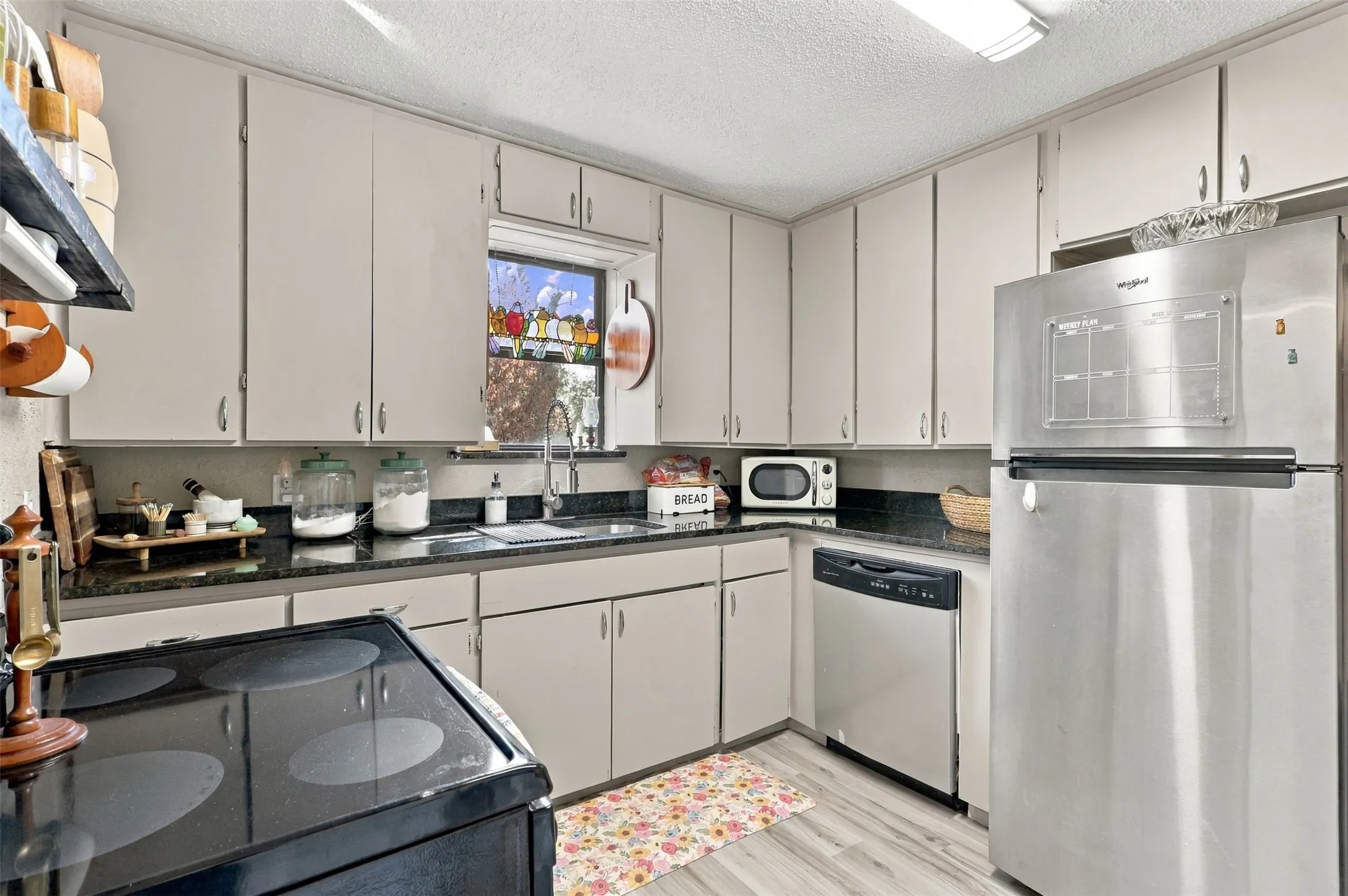 Kitchen featuring light-toned cabinetry, dark granite-style countertops, stainless steel refrigerator, stainless steel dishwasher, and wood-finish flooring