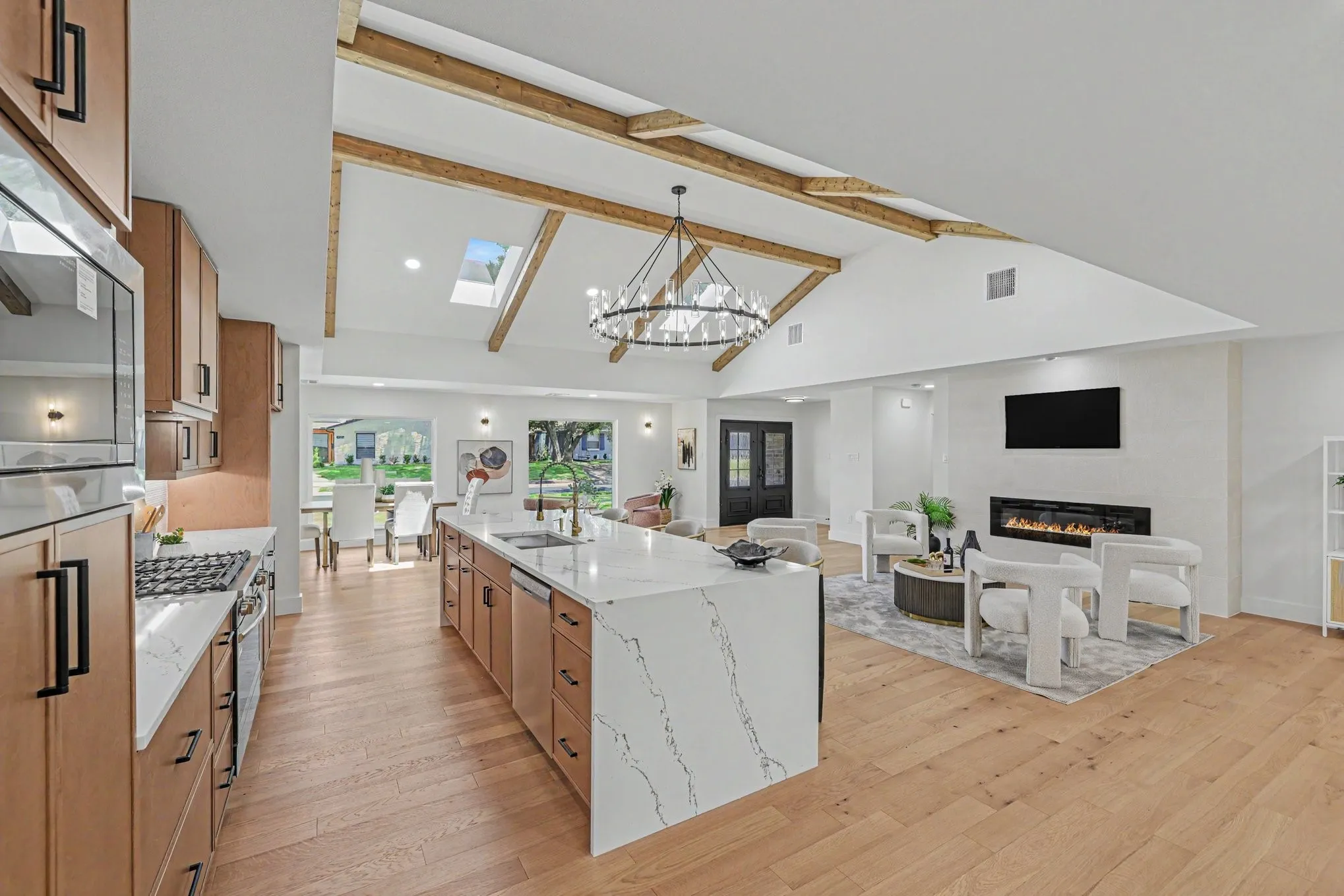 Vaulted ceilings with exposed wood beams, skylights, wood-finish flooring, a kitchen island with a waterfall countertop, and an integrated fireplace