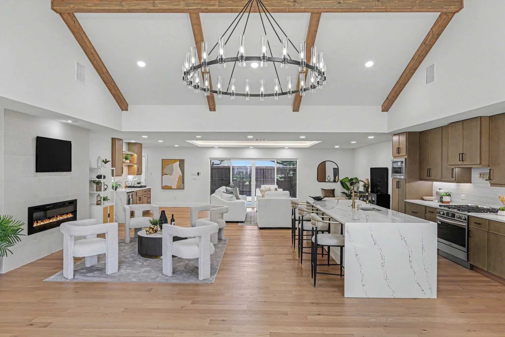 Vaulted ceiling with exposed wood beams, wood-finish flooring, built-in electric fireplace, recessed lighting, and a kitchen island with stone countertops