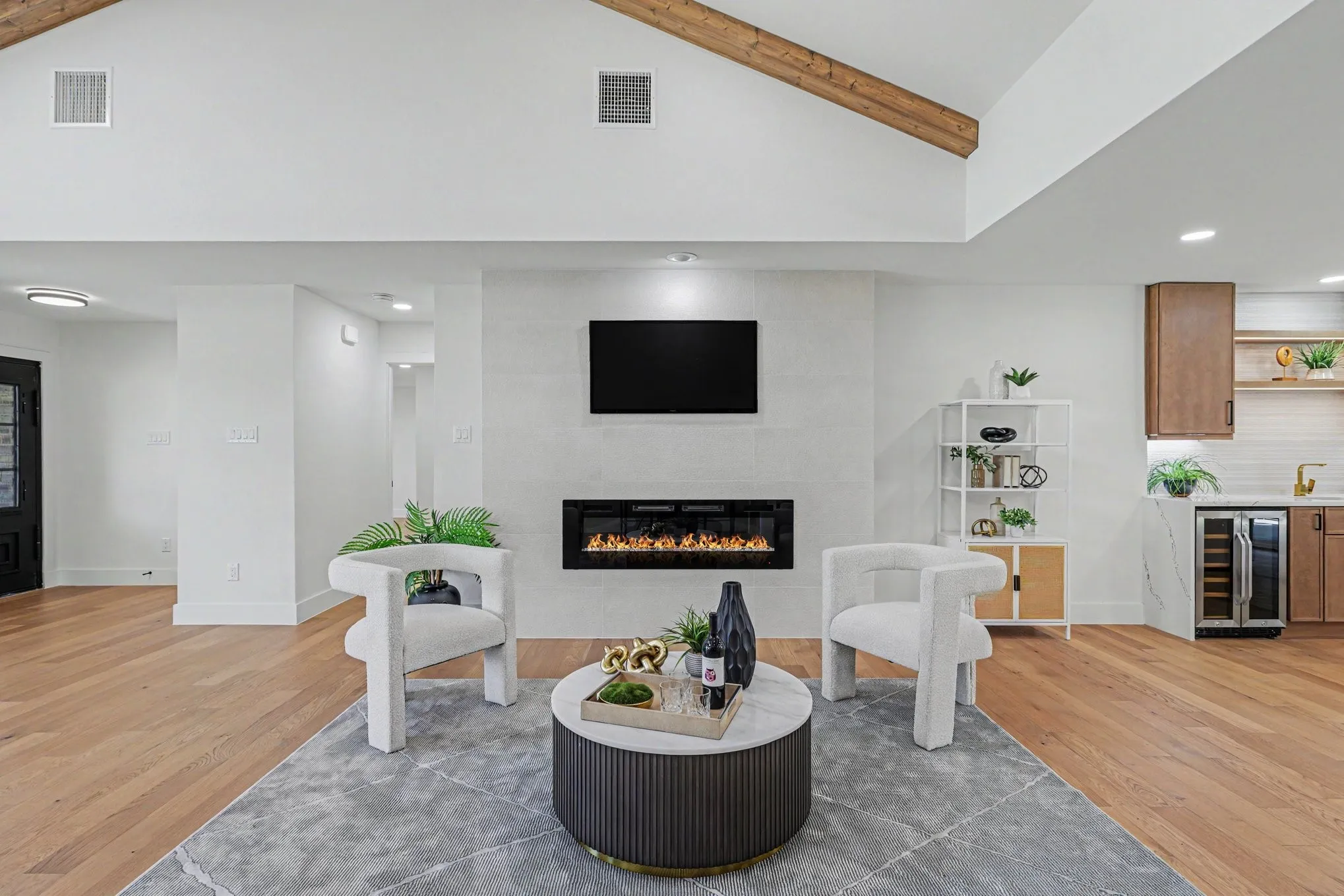 Hardwood flooring, vaulted ceiling with exposed wood beams, wall-mounted electric fireplace, and a built-in beverage cooler