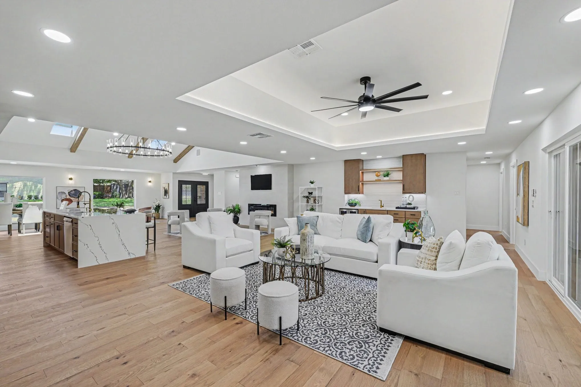 Wood-finish flooring throughout, tray ceiling with recessed lighting, kitchen island with waterfall countertop, built-in wet bar, and sliding glass doors
