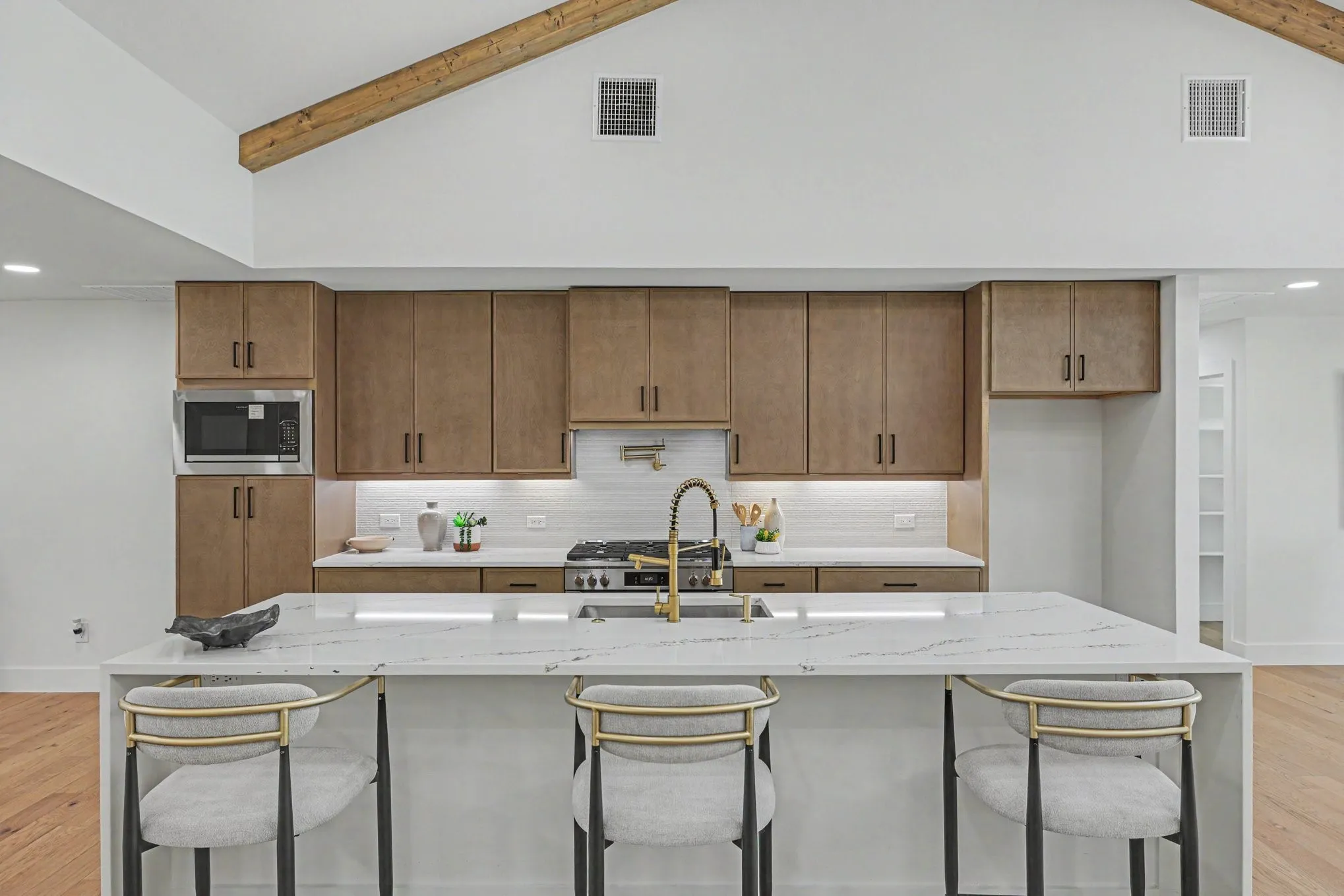 Vaulted ceiling with exposed wood beam, wood-finish cabinetry, white subway tile backsplash, white countertop island, and stainless steel appliances