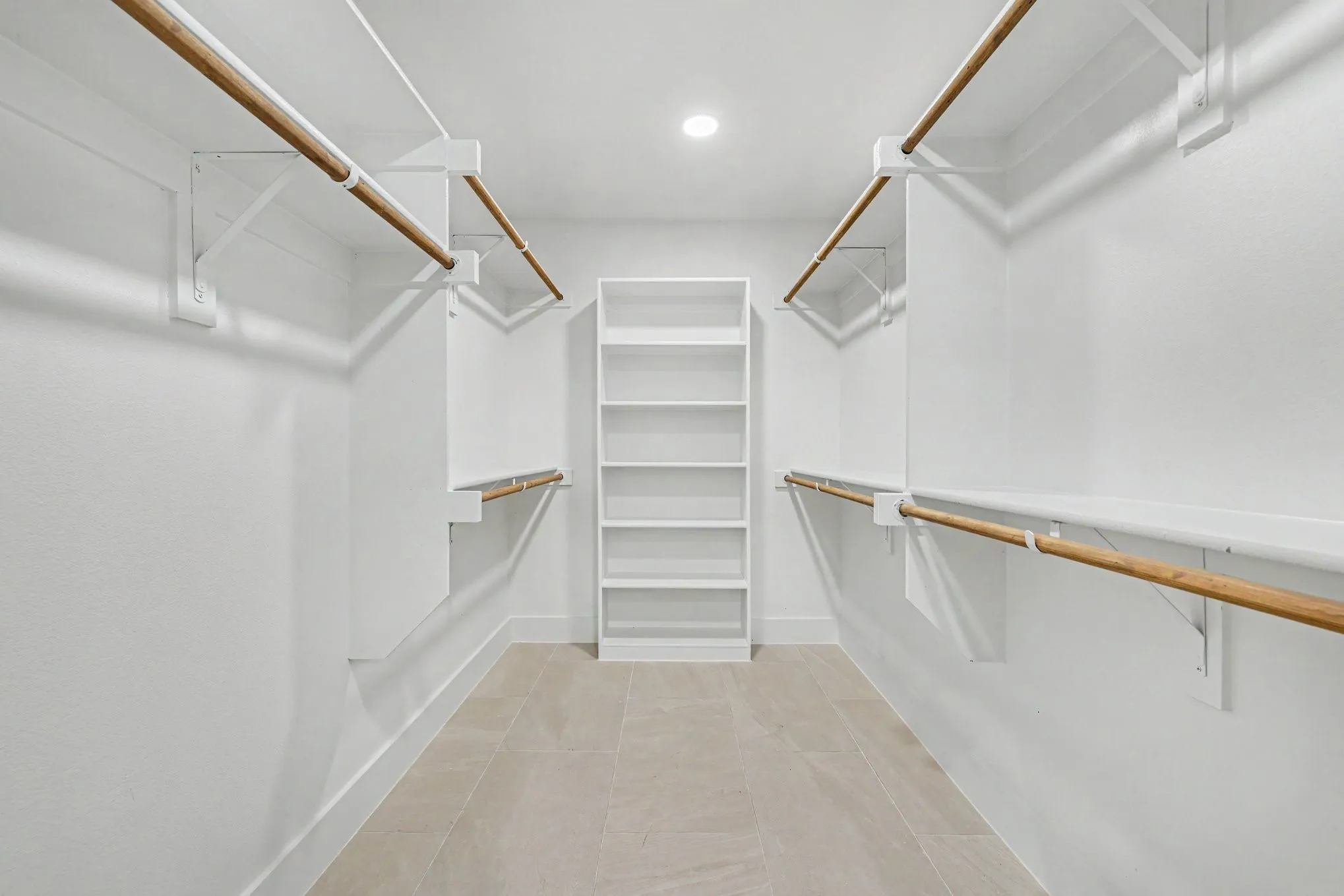 Integrated shelving system with multiple hanging rods, built-in open shelving, recessed ceiling light, and light-toned tile flooring