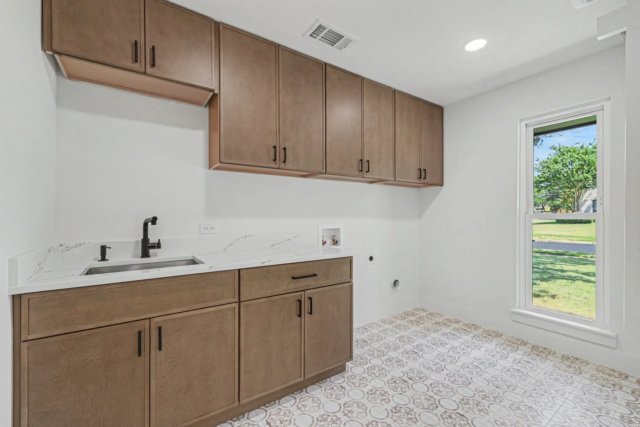 Functional utility room featuring extensive built-in cabinetry, a sink with a matte black faucet, light-toned countertops, and decorative floor tiling