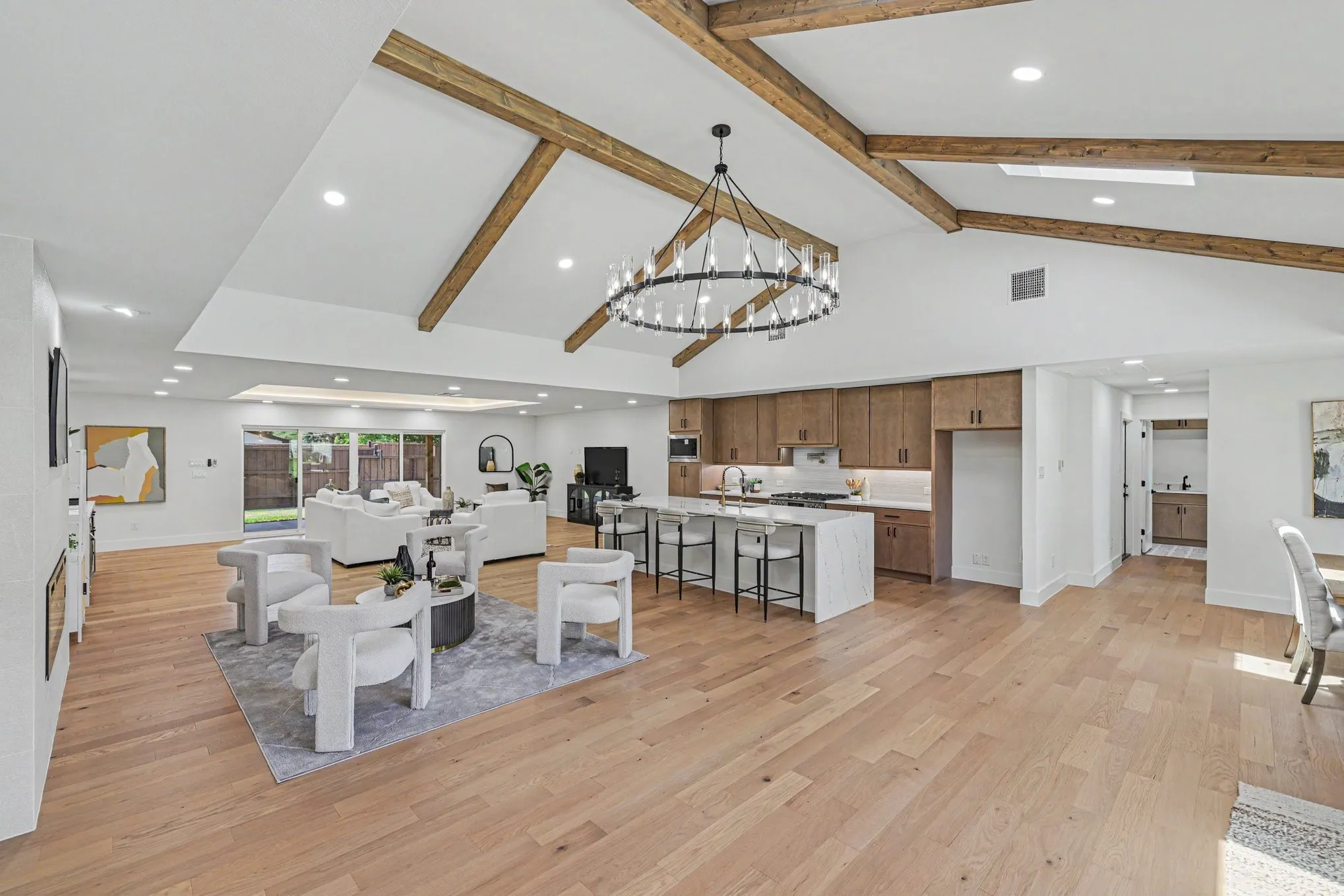 Vaulted ceilings with exposed beams, recessed lighting, wood-finish flooring, a kitchen island with seating, and sliding glass doors