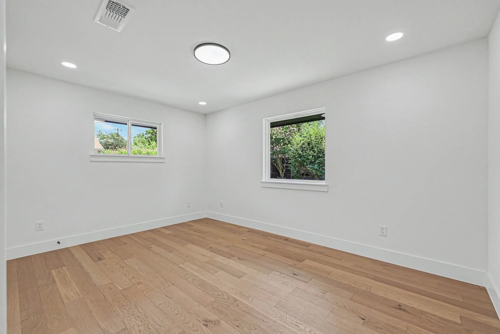 Wood-finish flooring, recessed lighting, and two windows with white trim
